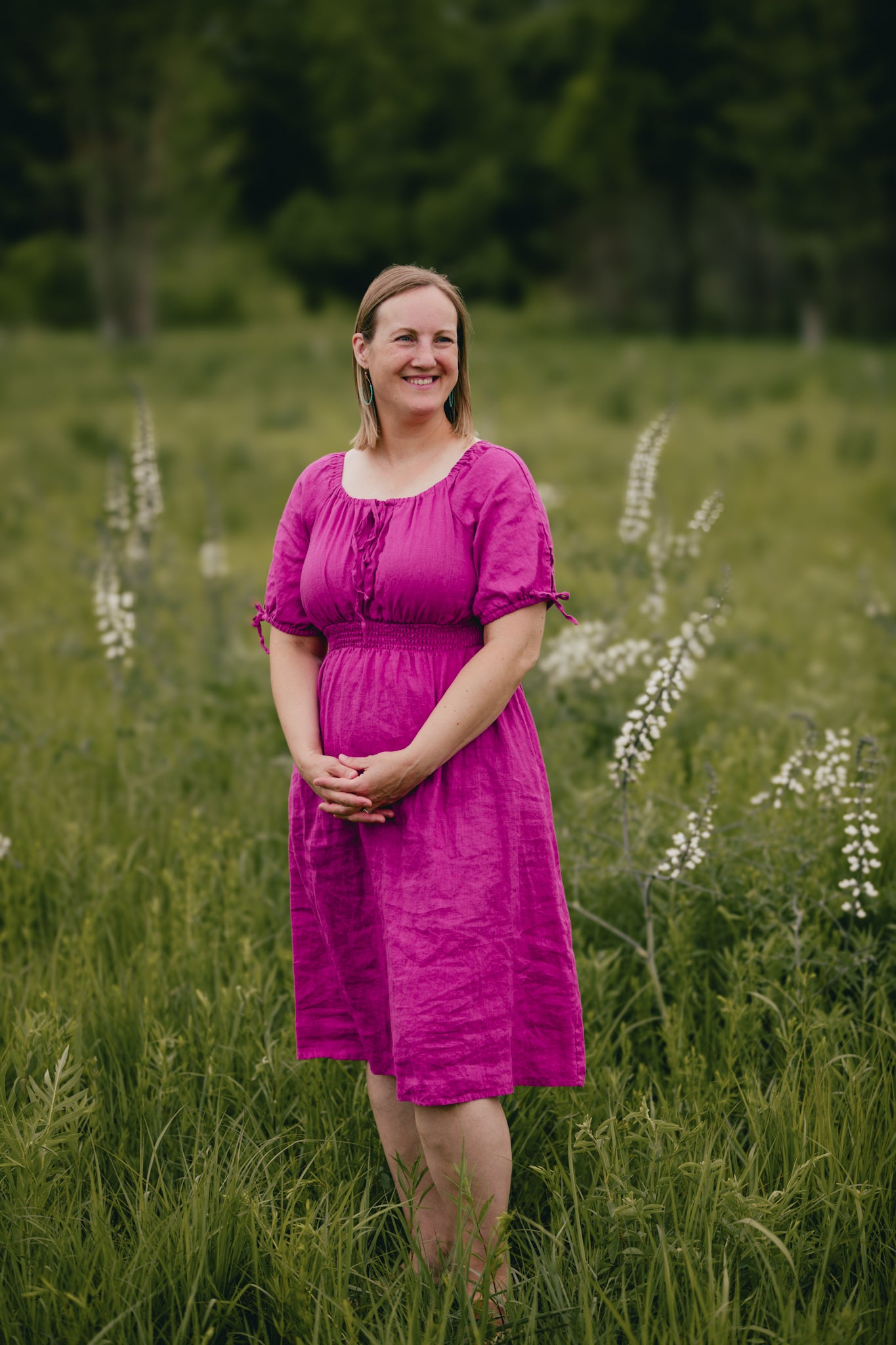 Woman in a pink modest nursing dress standing in a field with greenery and flowers.