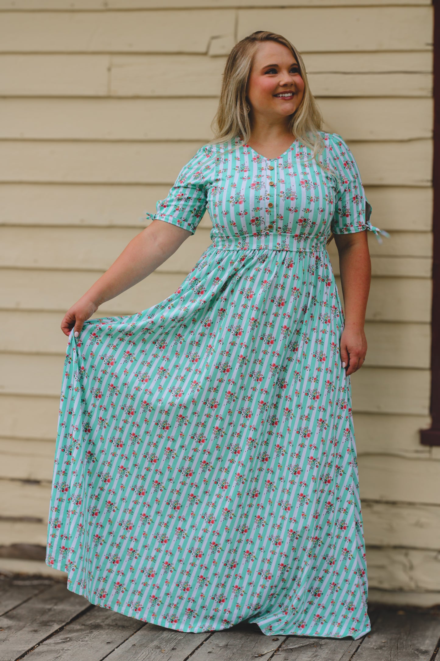 Woman wearing a floral modest nursing dress standing in front of a wooden wall.