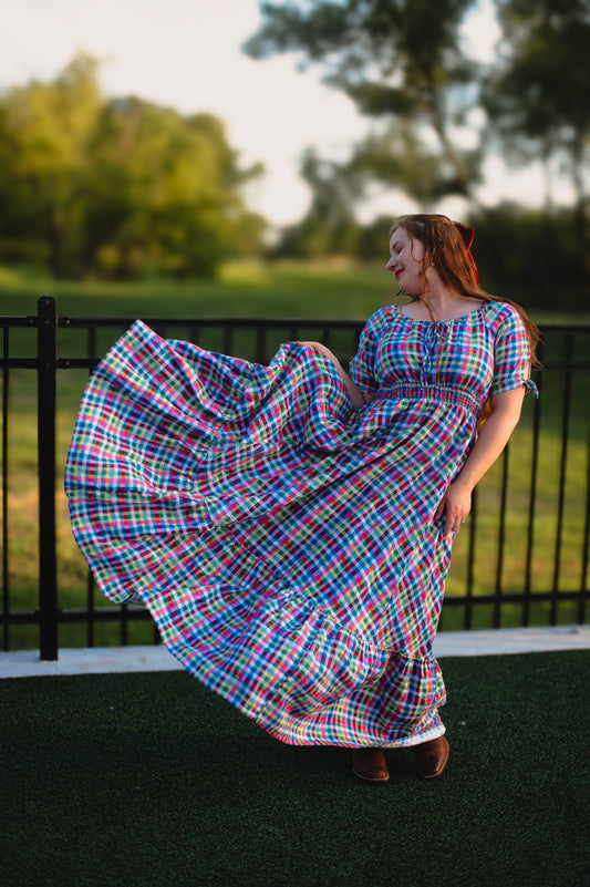 Woman in a colorful plaid modest nursing dress standing outdoors with trees in the background