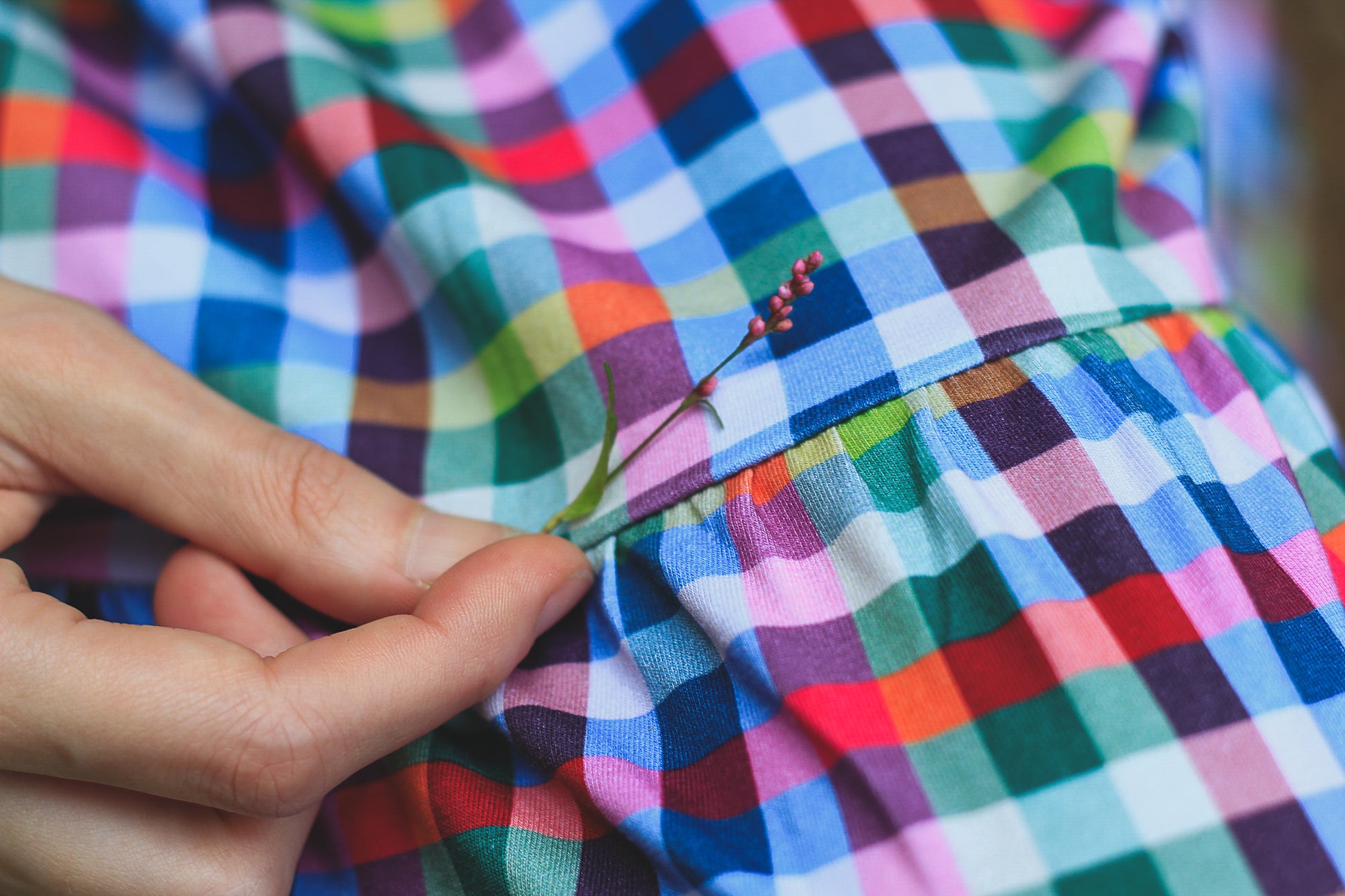 Colorful checkered fabric with a hand sewing a button.