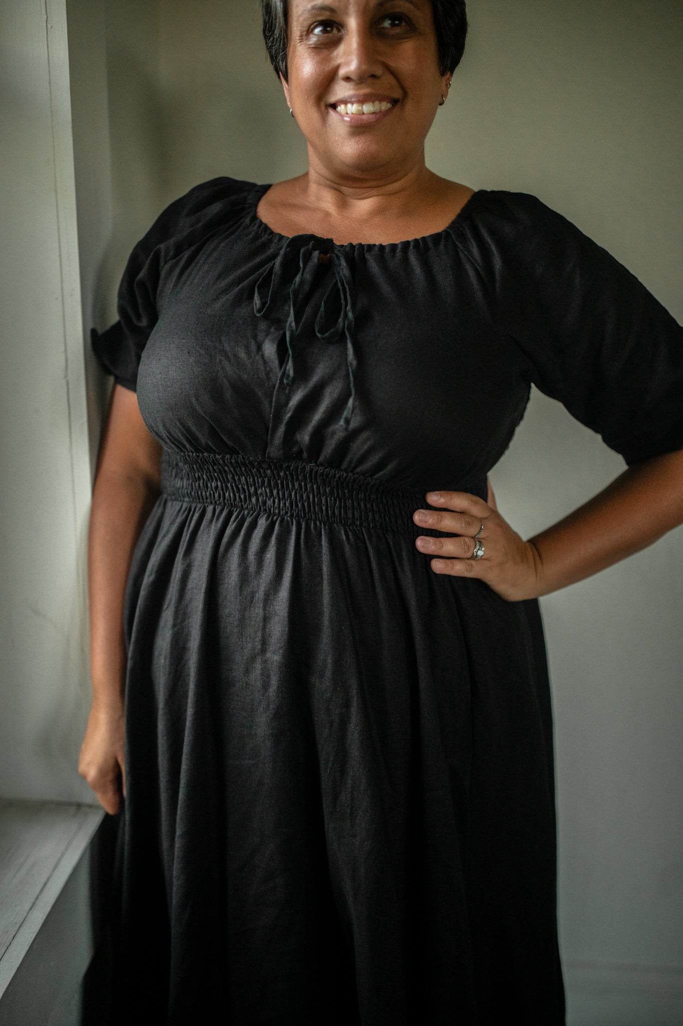 Woman wearing a black modest nursing dress standing against a plain wall.