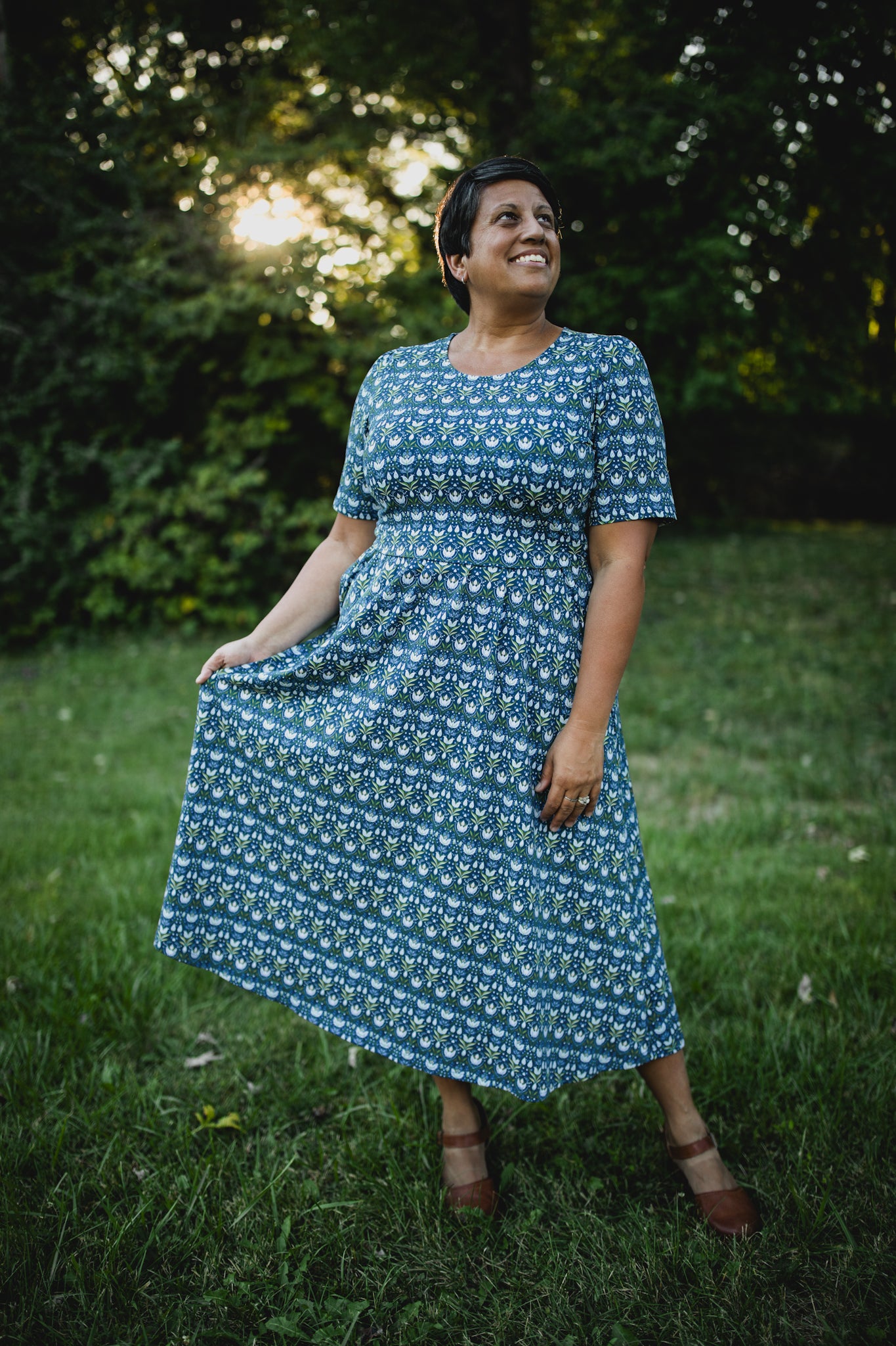 Woman in modest nursing dress, outdoors greenery background.