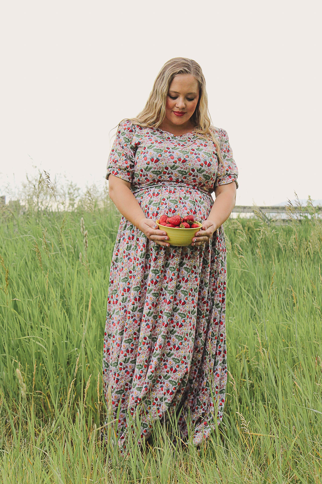 Woman in a floral modest nursing dress holding a basket of fruit in a grassy field