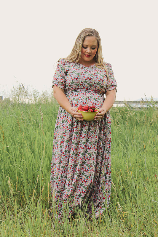 Woman in a floral modest nursing dress holding a basket of fruit in a grassy field
