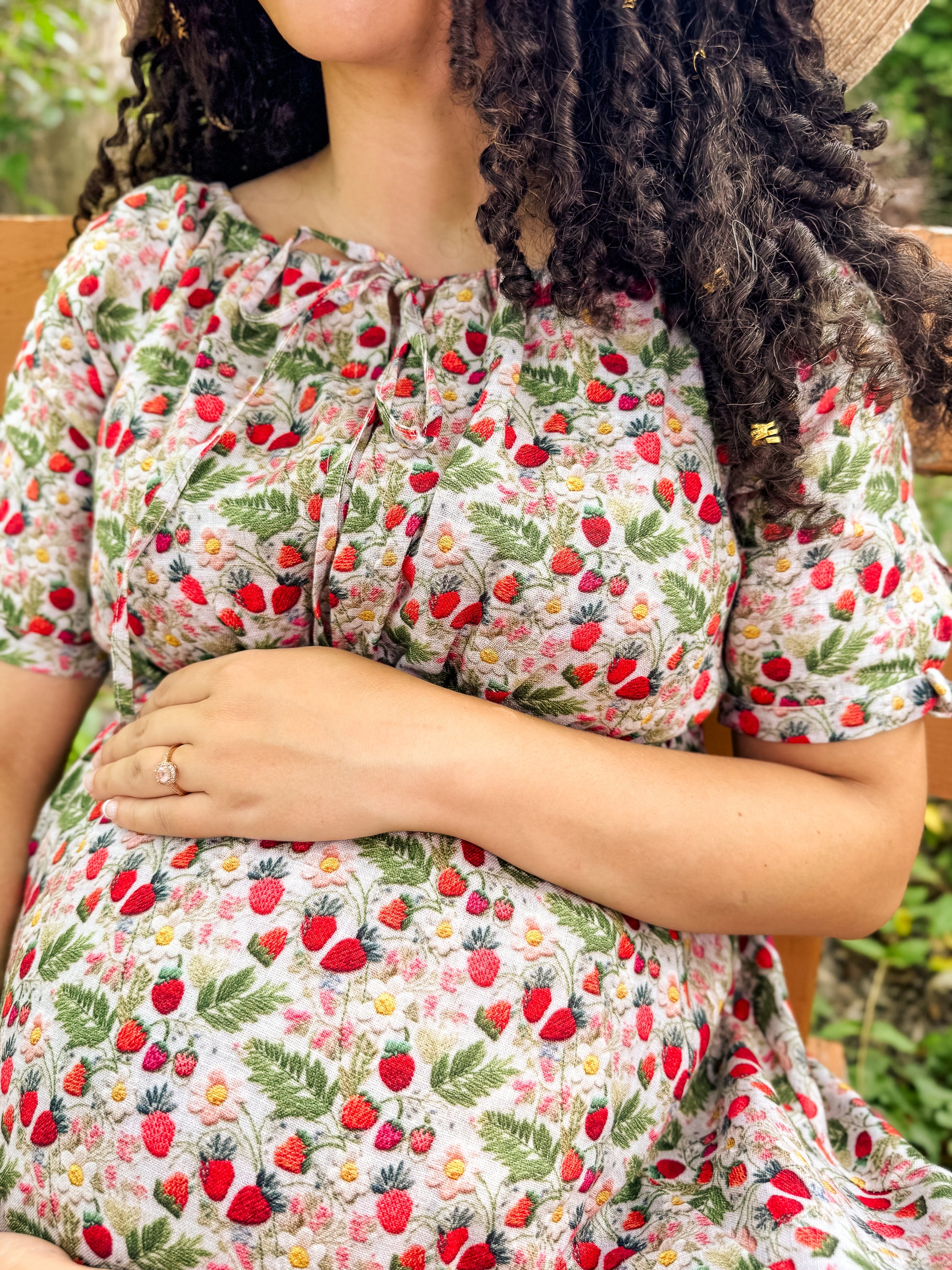 Person wearing a floral modest nursing dress with red strawberries and green leaves.