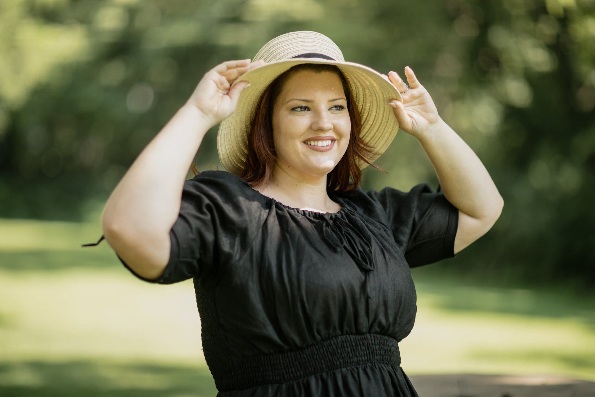 Woman wearing a black modest nursing dress and straw hat outdoors