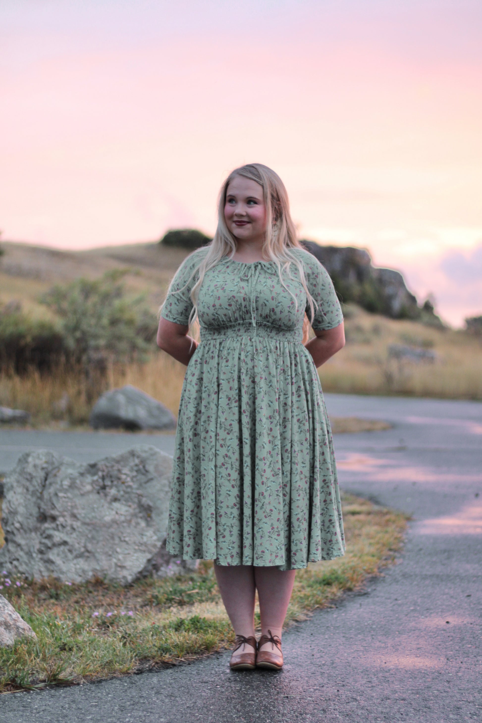 Woman in a green dress standing on a path with a scenic background
