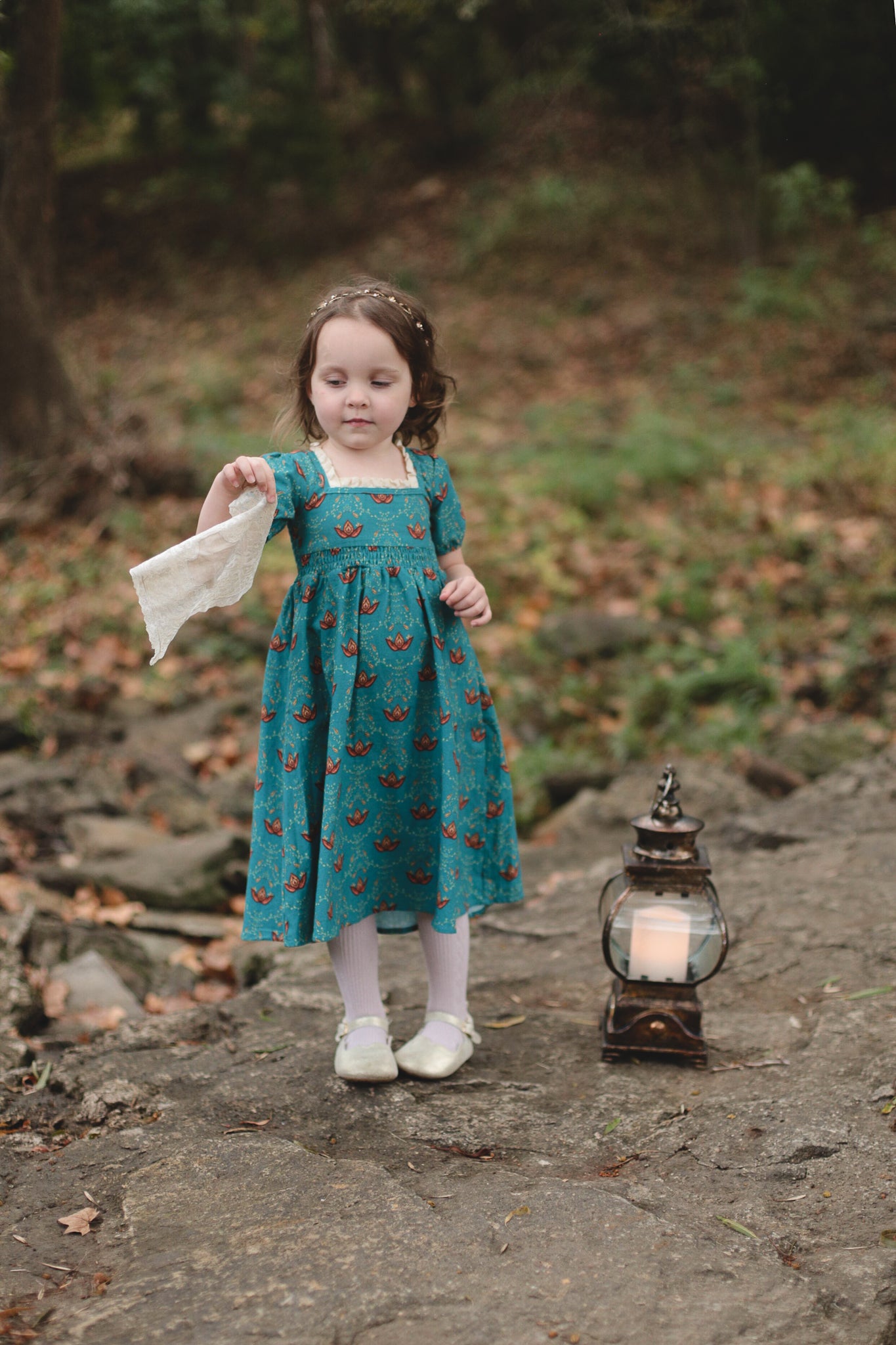Young girl wearing modest dress with lantern outdoors.