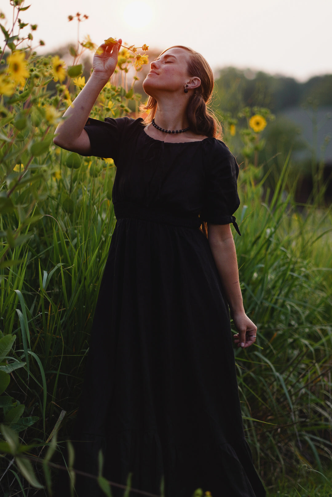 Woman in a black modest nursing dress standing in a field of sunflowers