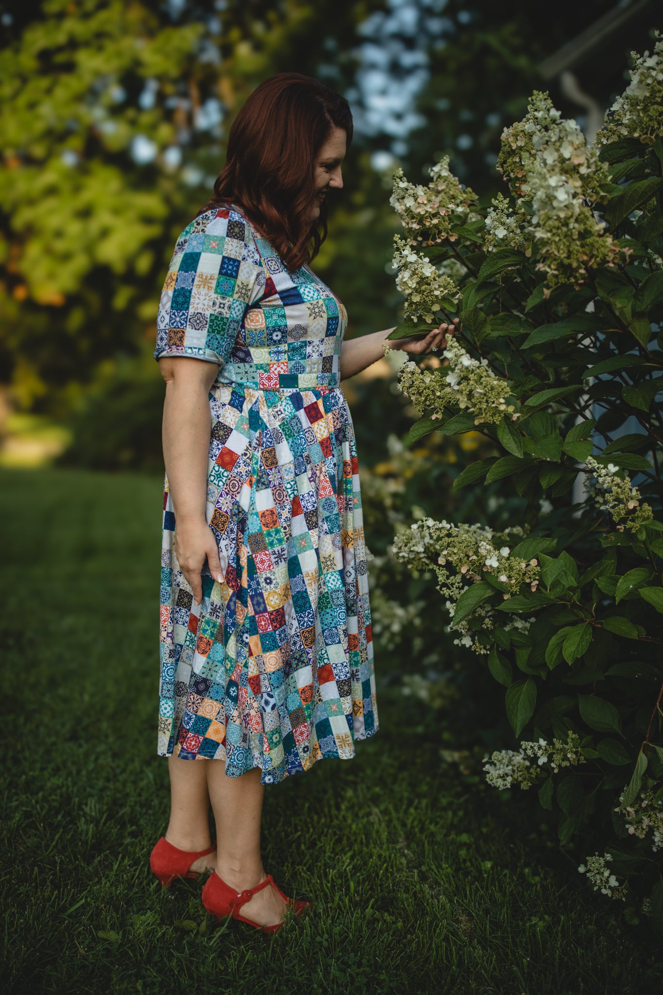 Woman in a colorful patchwork modest nursing dress standing in a garden.