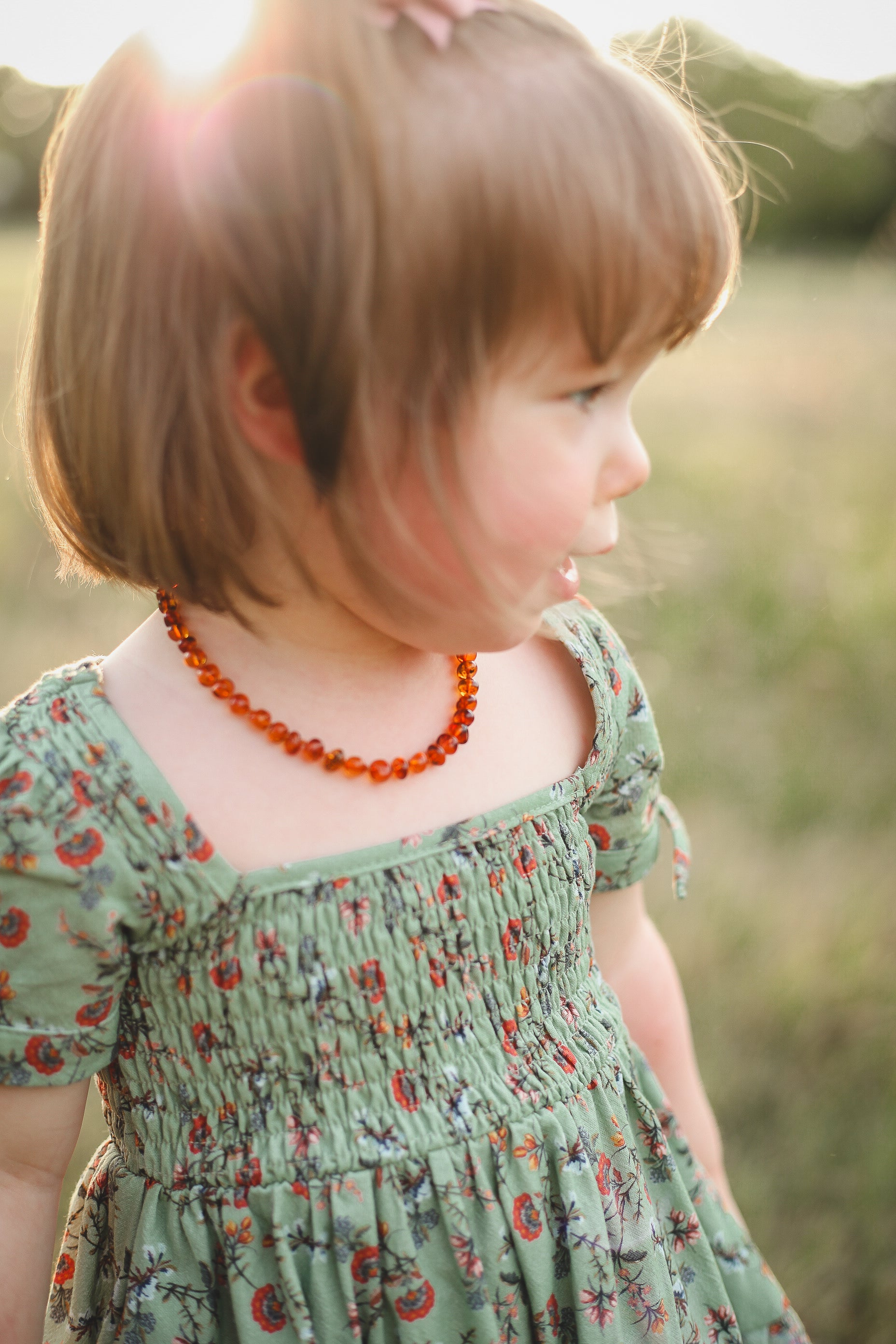 Child wearing a green floral dress and orange necklace in a natural setting