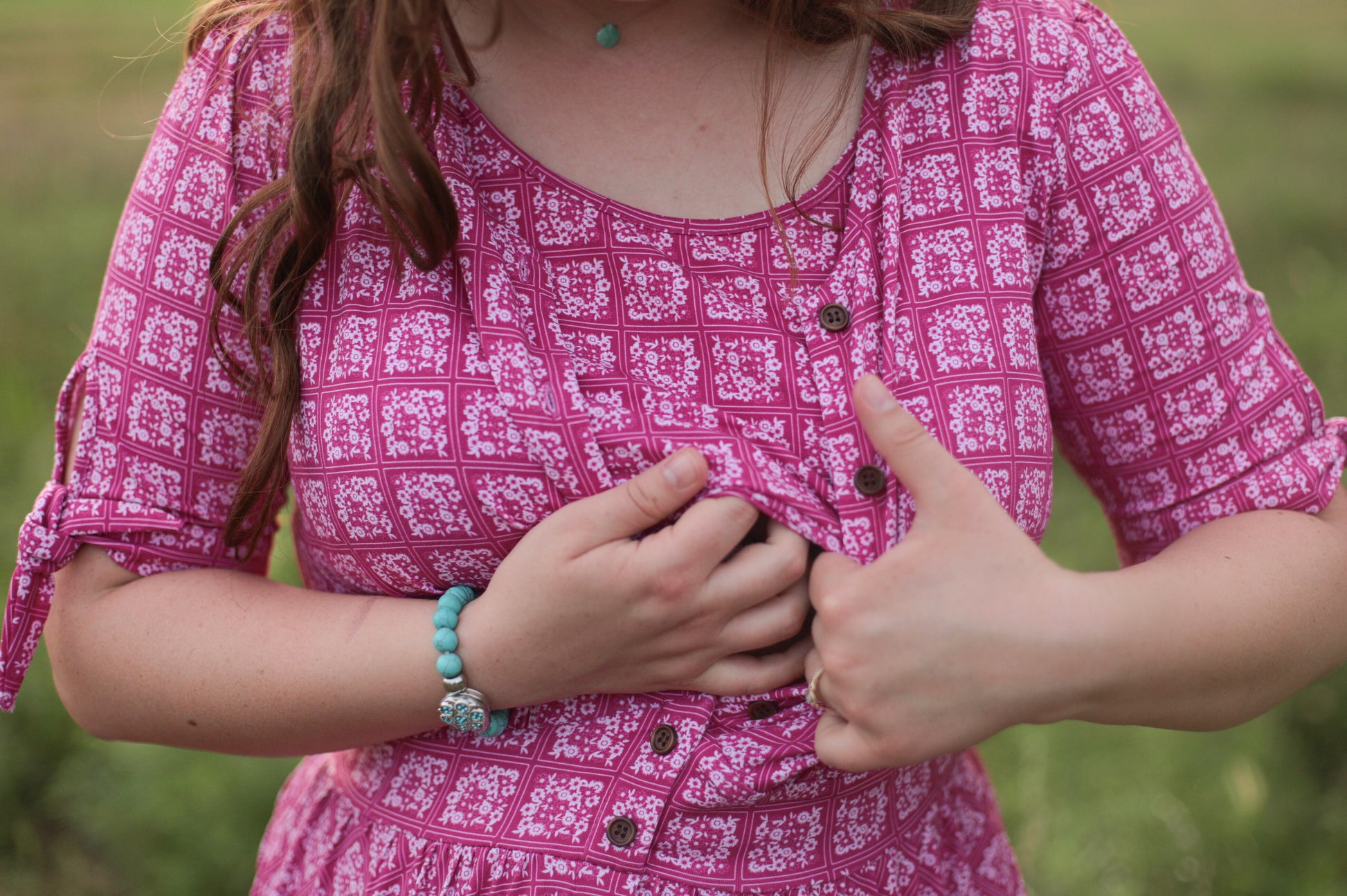 Person wearing a pink patterned modest nursing dress with a blurred green background