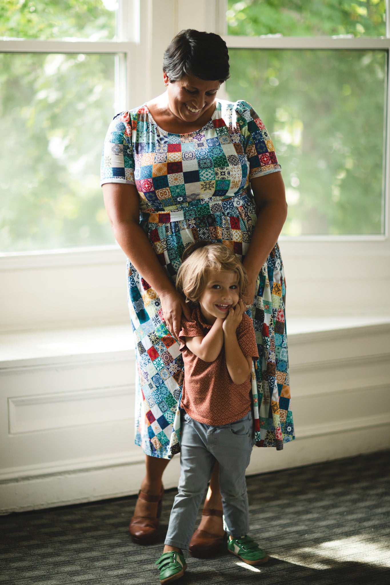 Woman in a colorful modest nursing dress holding a child by a window with natural light