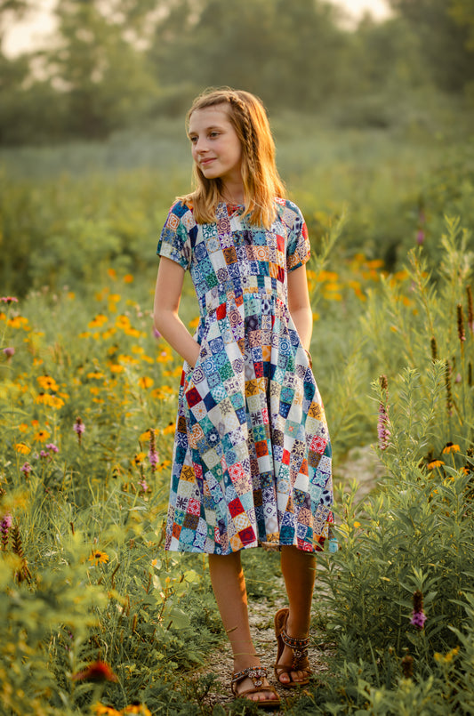 Woman in a colorful patchwork modest dress standing in a field of wildflowers