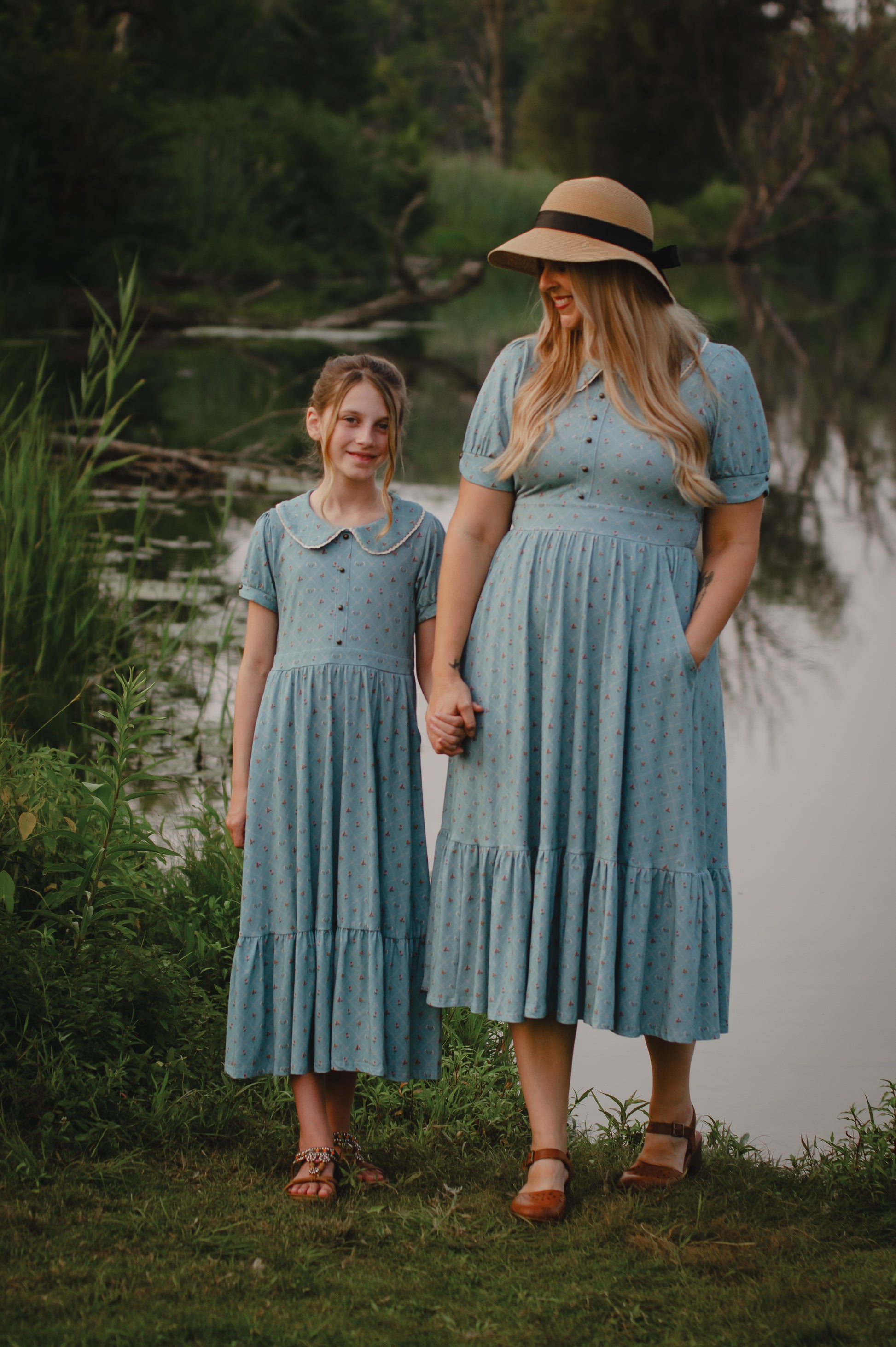 Mother and daughter in matching modest dresses standing by a body of water.
