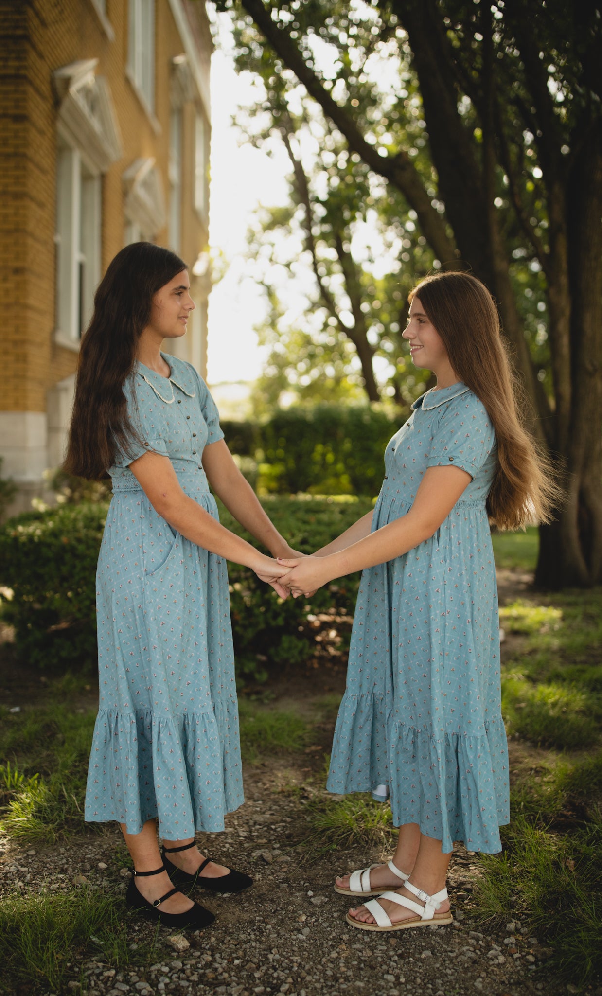 Two women in matching blue modest dresses holding hands outdoors.