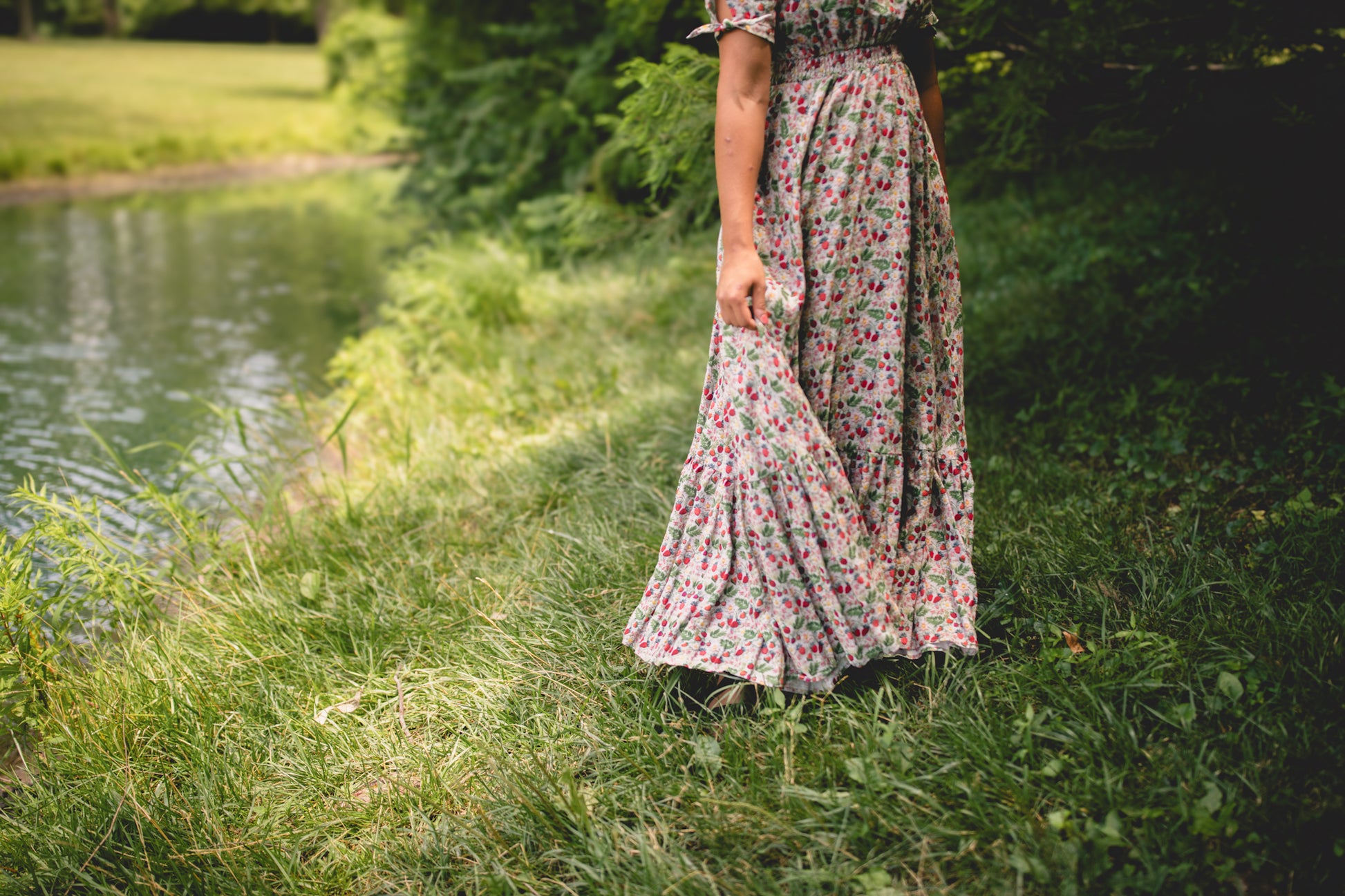 Person wearing a floral modest nursing dress standing by a body of water with greenery.