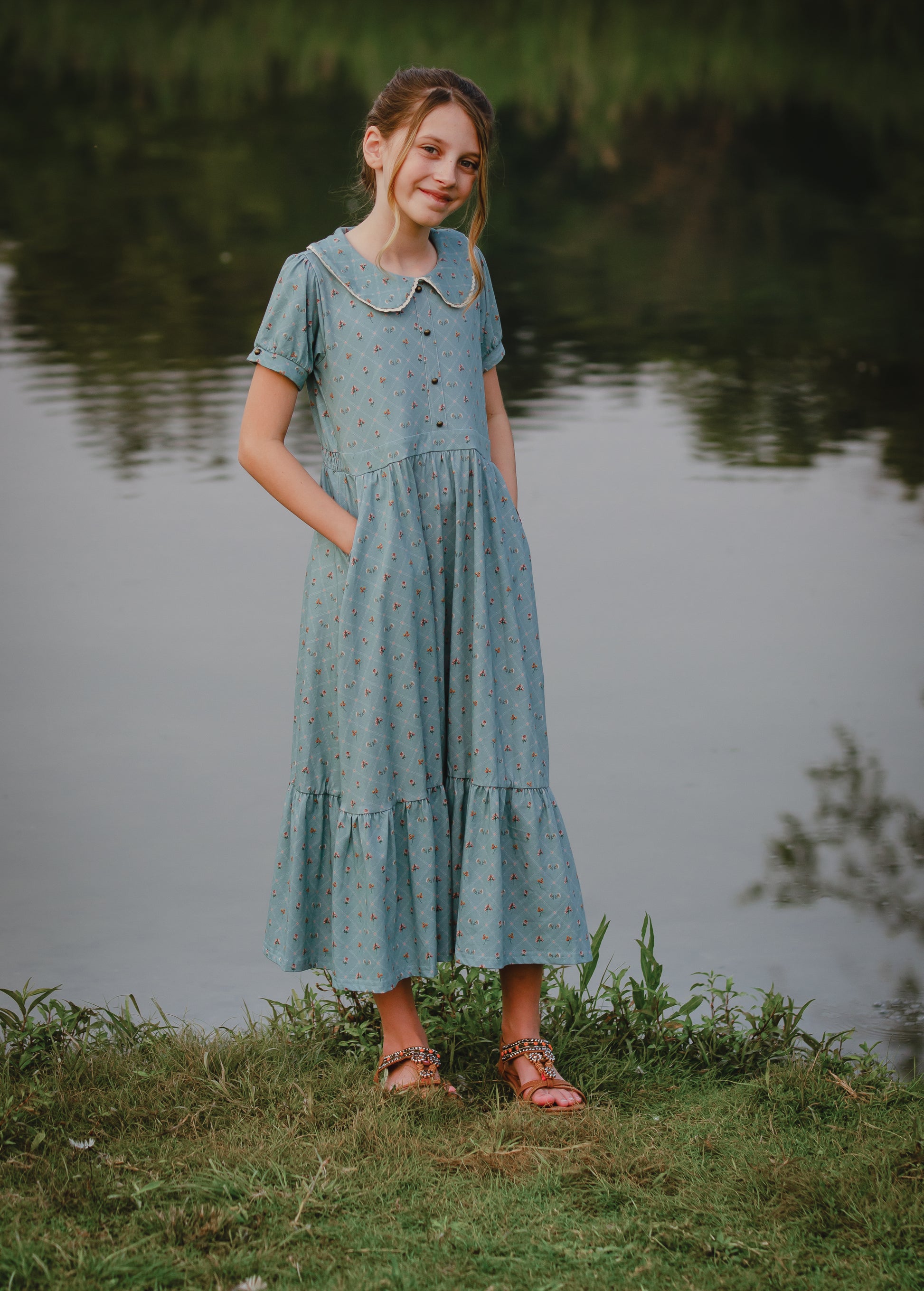 Young girl in a blue modest dress standing by a body of water