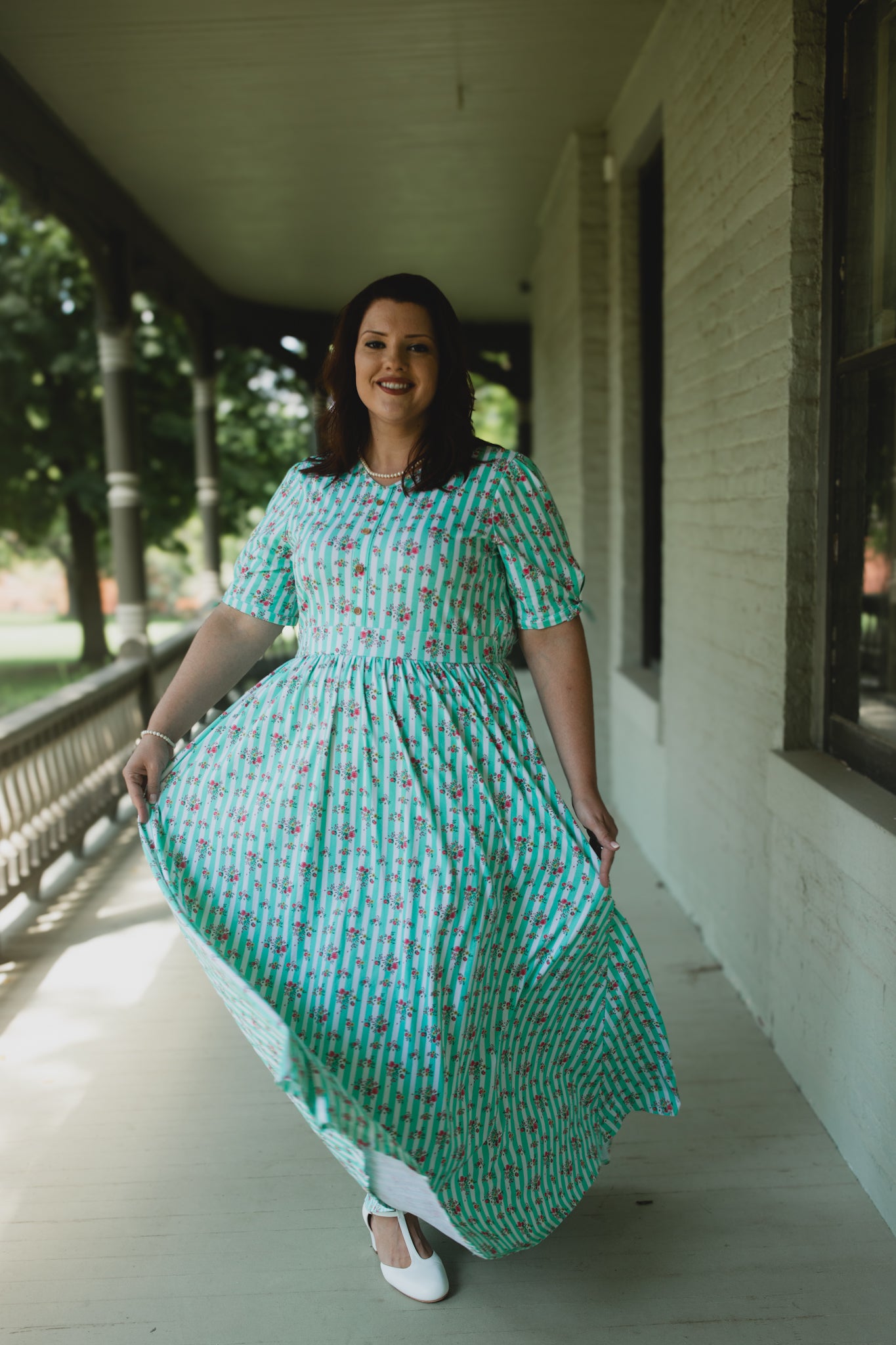 Woman in a green modest nursing dress standing on a porch