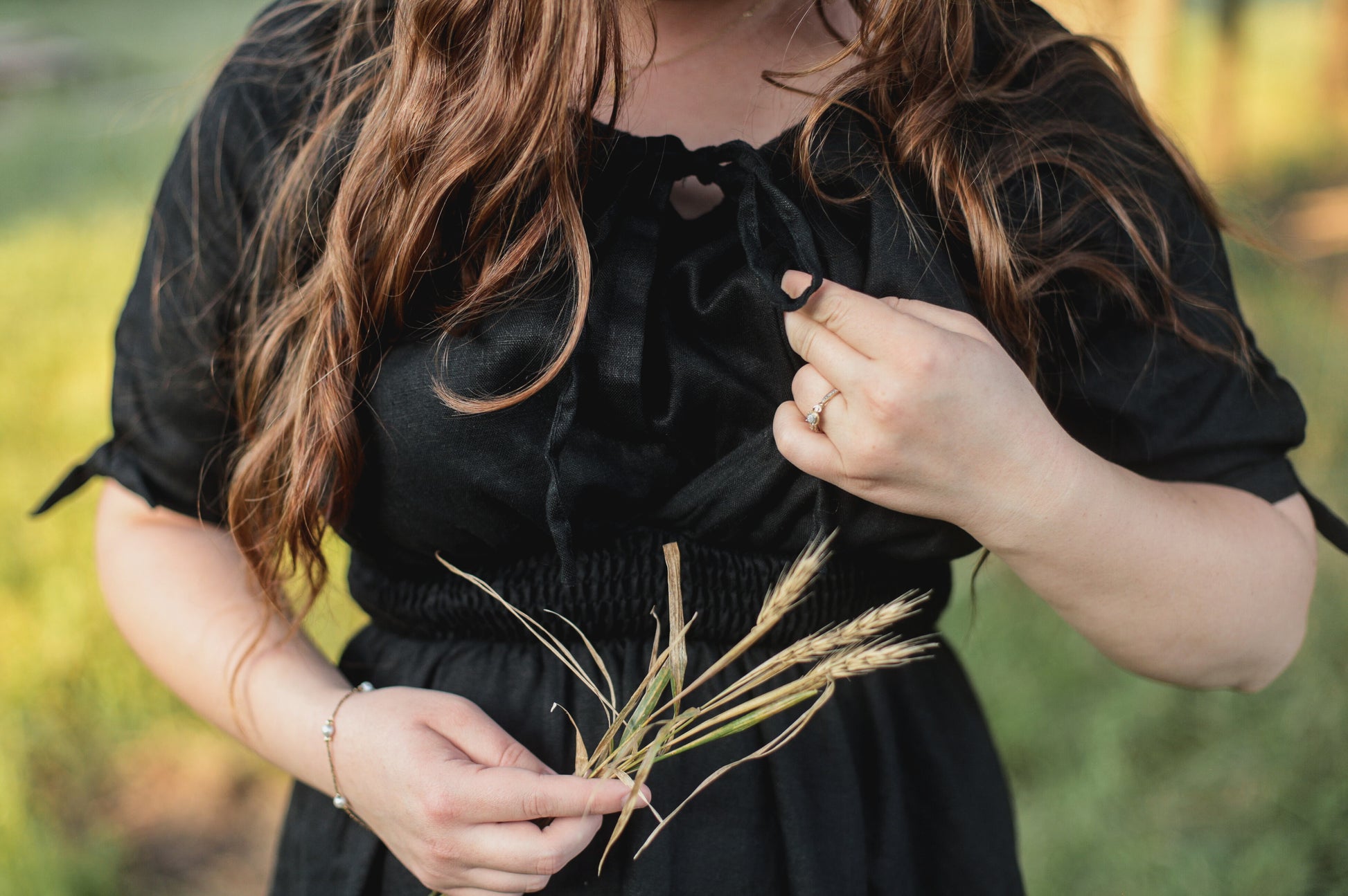 Person holding a bundle of grass in a natural setting wearing a modest nursing dress