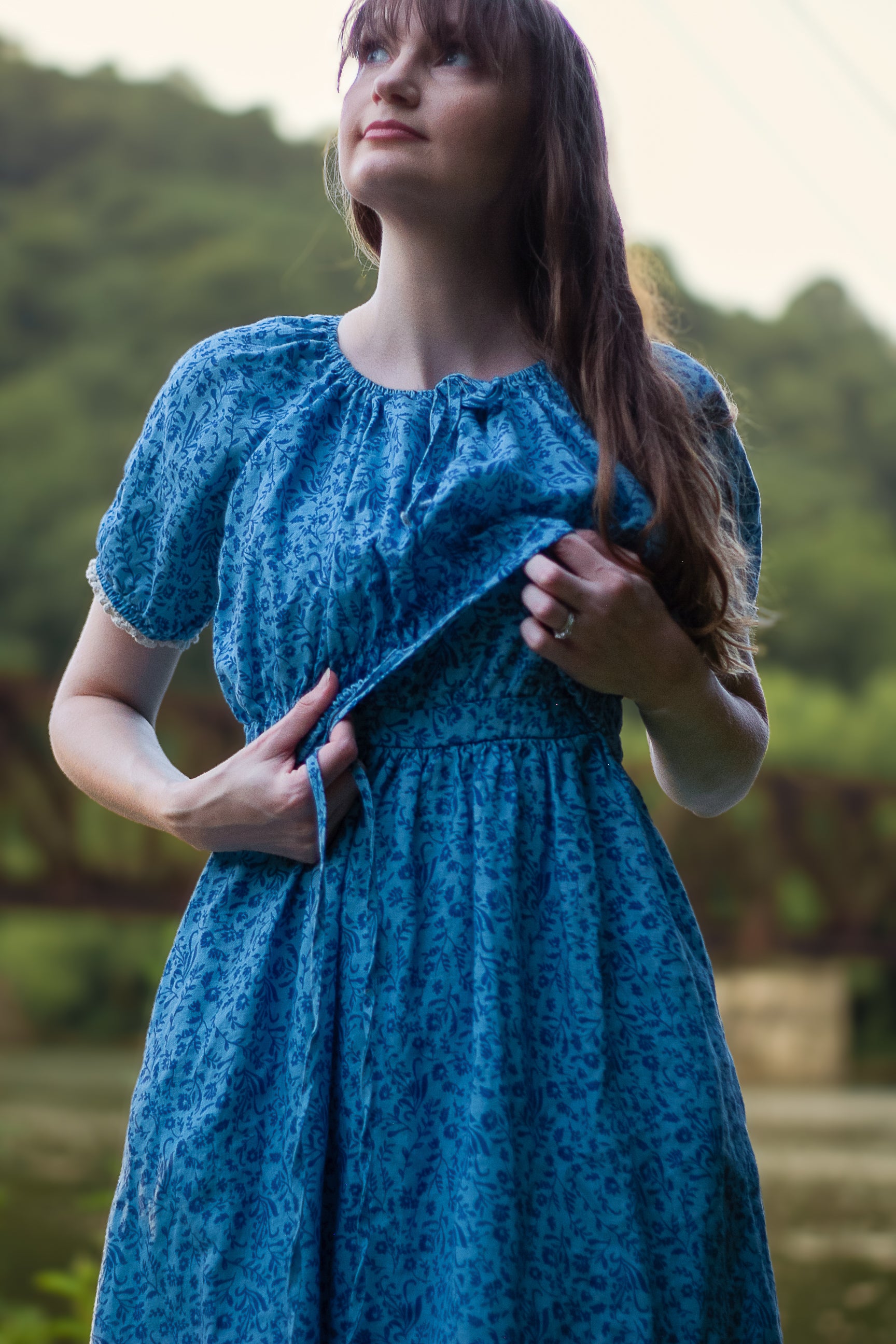 Woman wearing a blue modest nursing dress with a blurred natural background