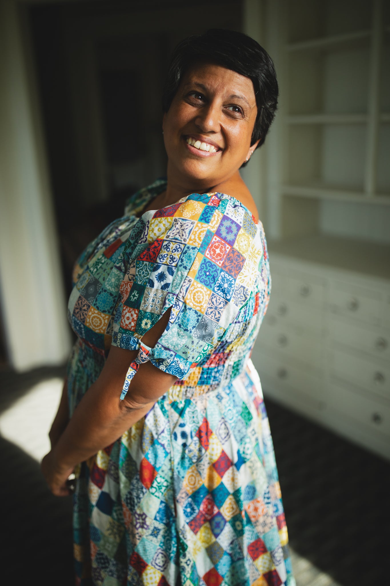 Woman wearing a colorful patterned modest nursing dress standing indoors.