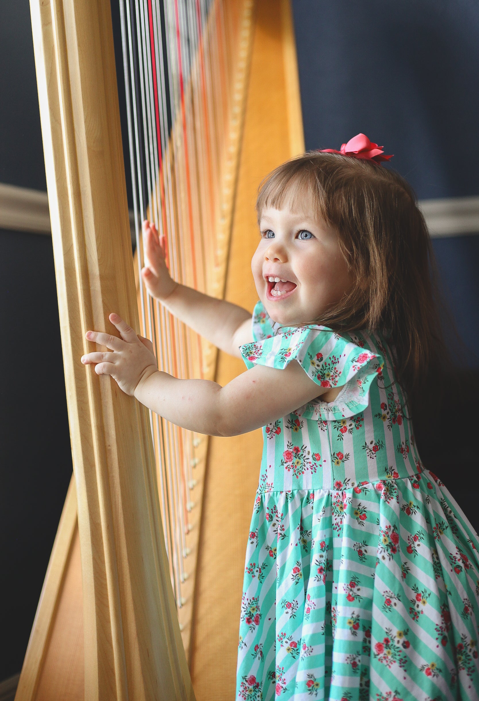 Child in a floral dress reaching out to touch a harp