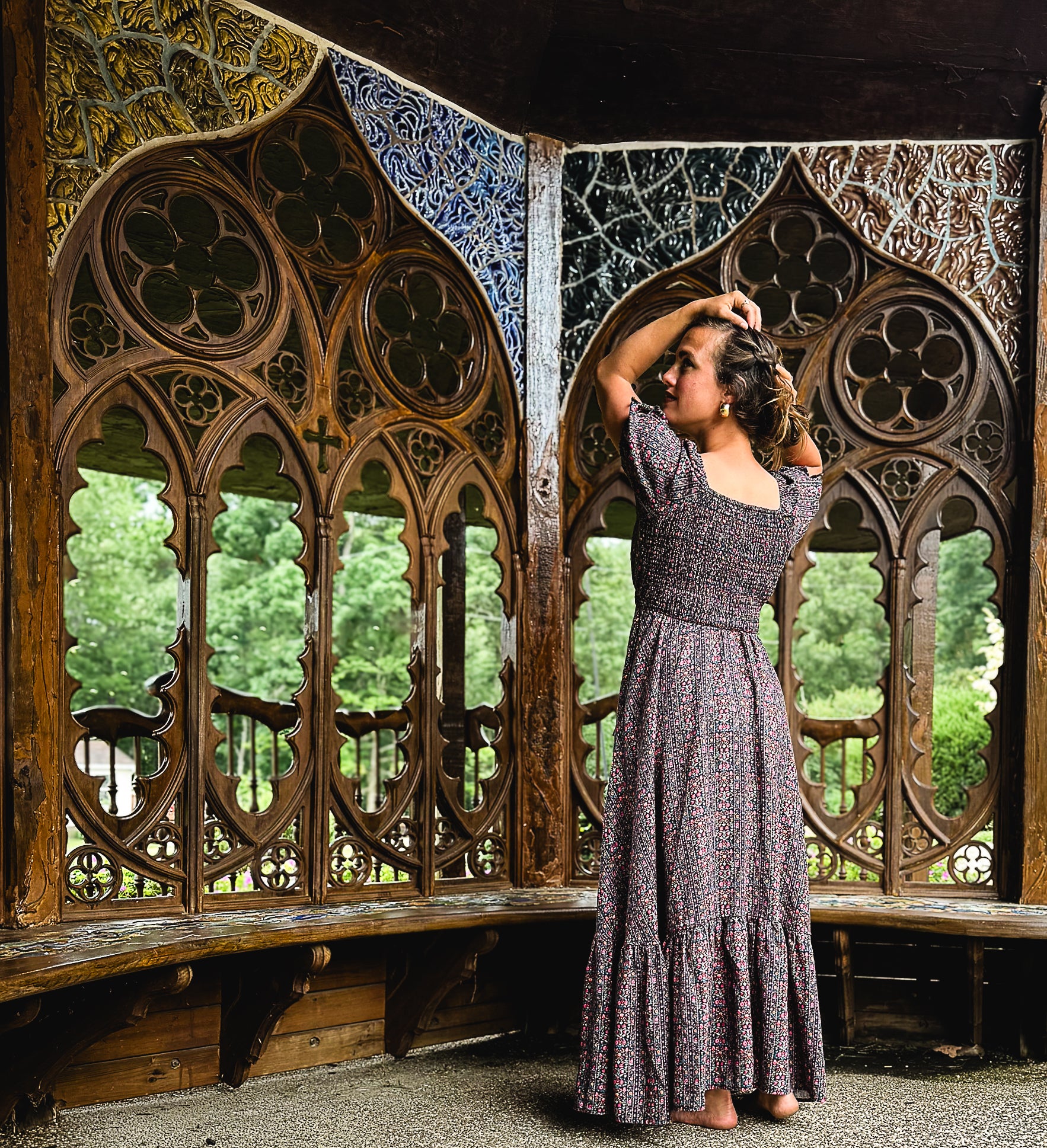 Woman in a long modest nursing dress standing in front of ornate wooden gothic-style windows.