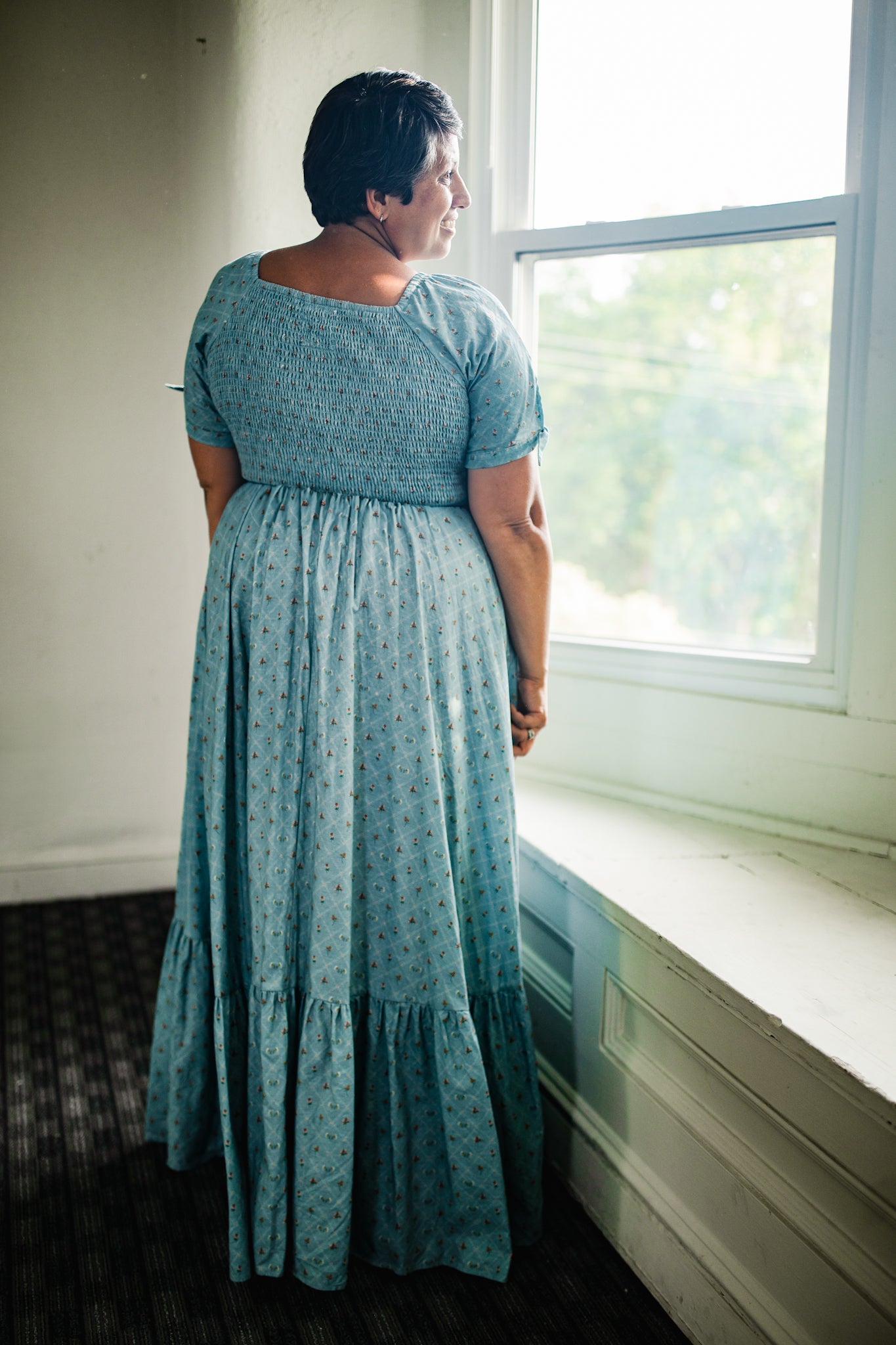 Person wearing a blue modest nursing dress standing by a window