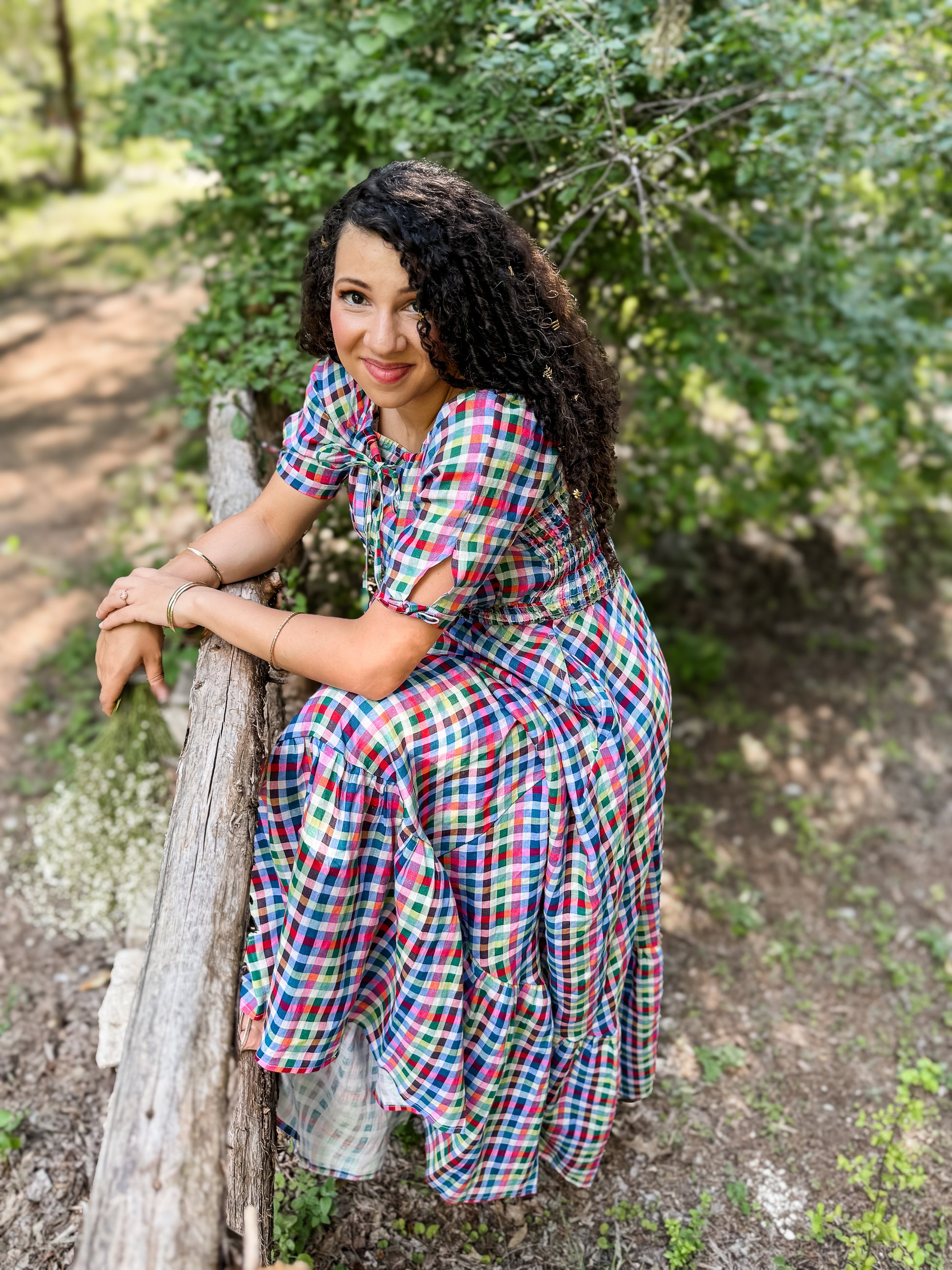 Woman in a colorful modest nursing dress sitting on a wooden log in a natural setting