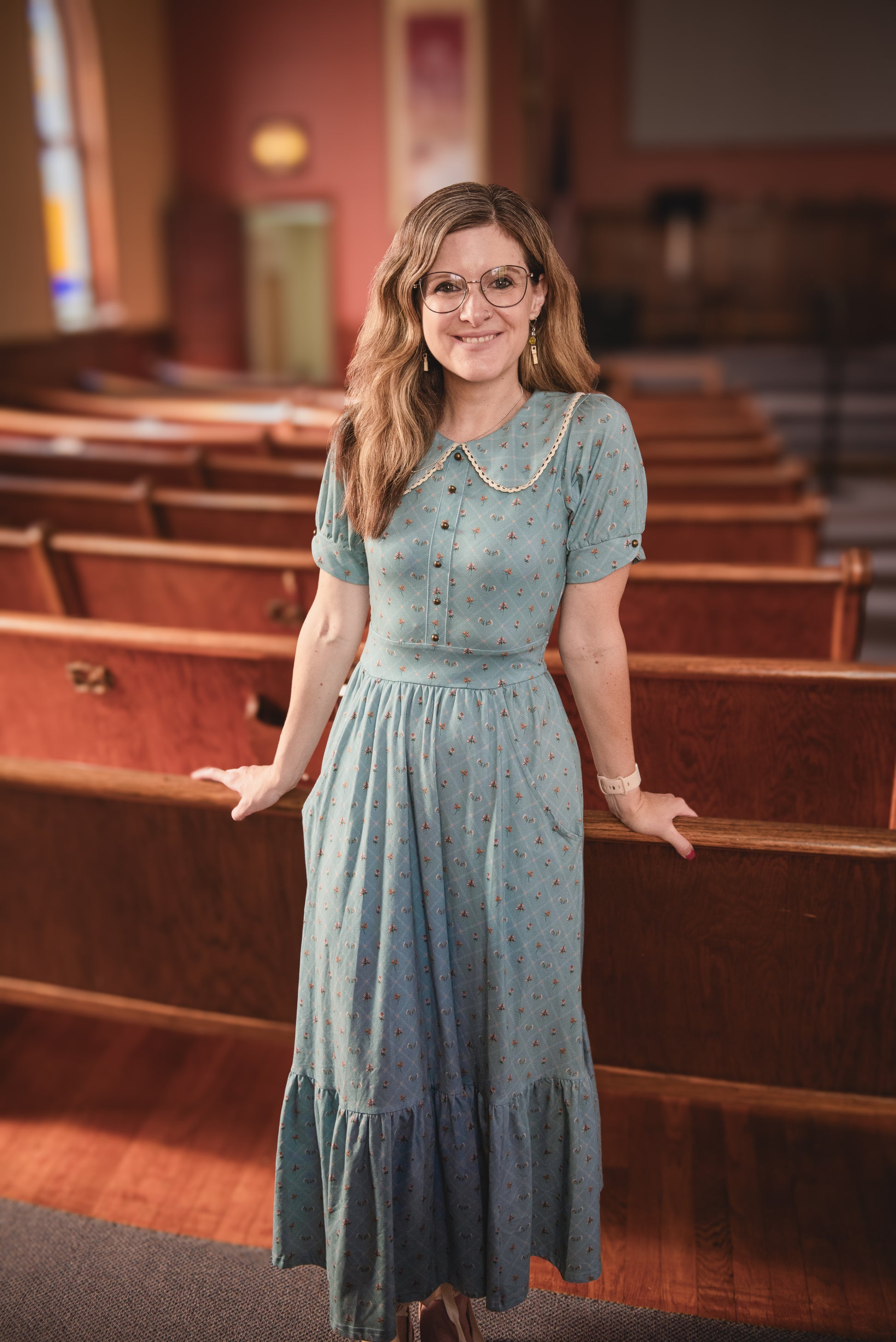 Woman in a light blue modest nursing dress standing in a church pew.