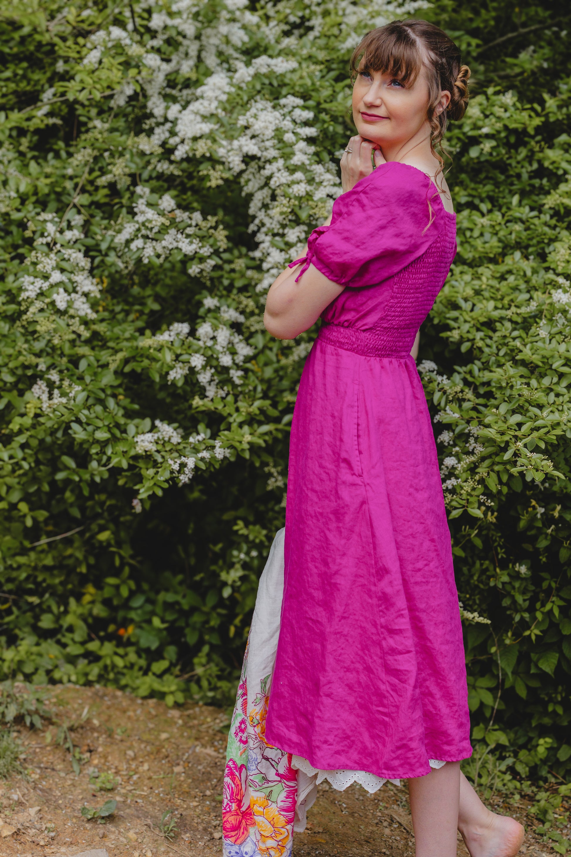 Woman in a bright pink modest nursing dress standing outdoors with greenery in the background