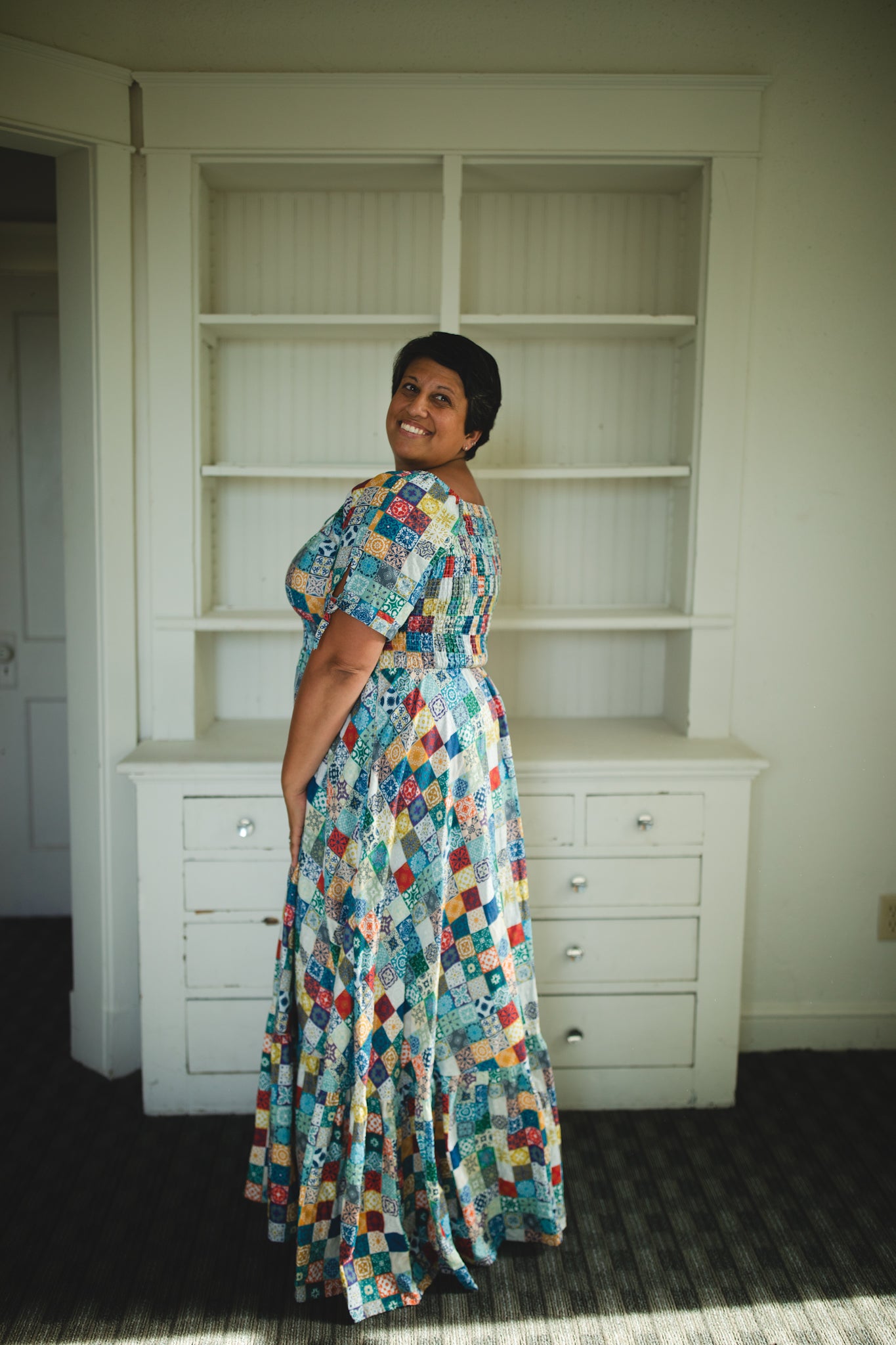 Woman in a colorful modest nursing dress standing in a room with white bookshelves.