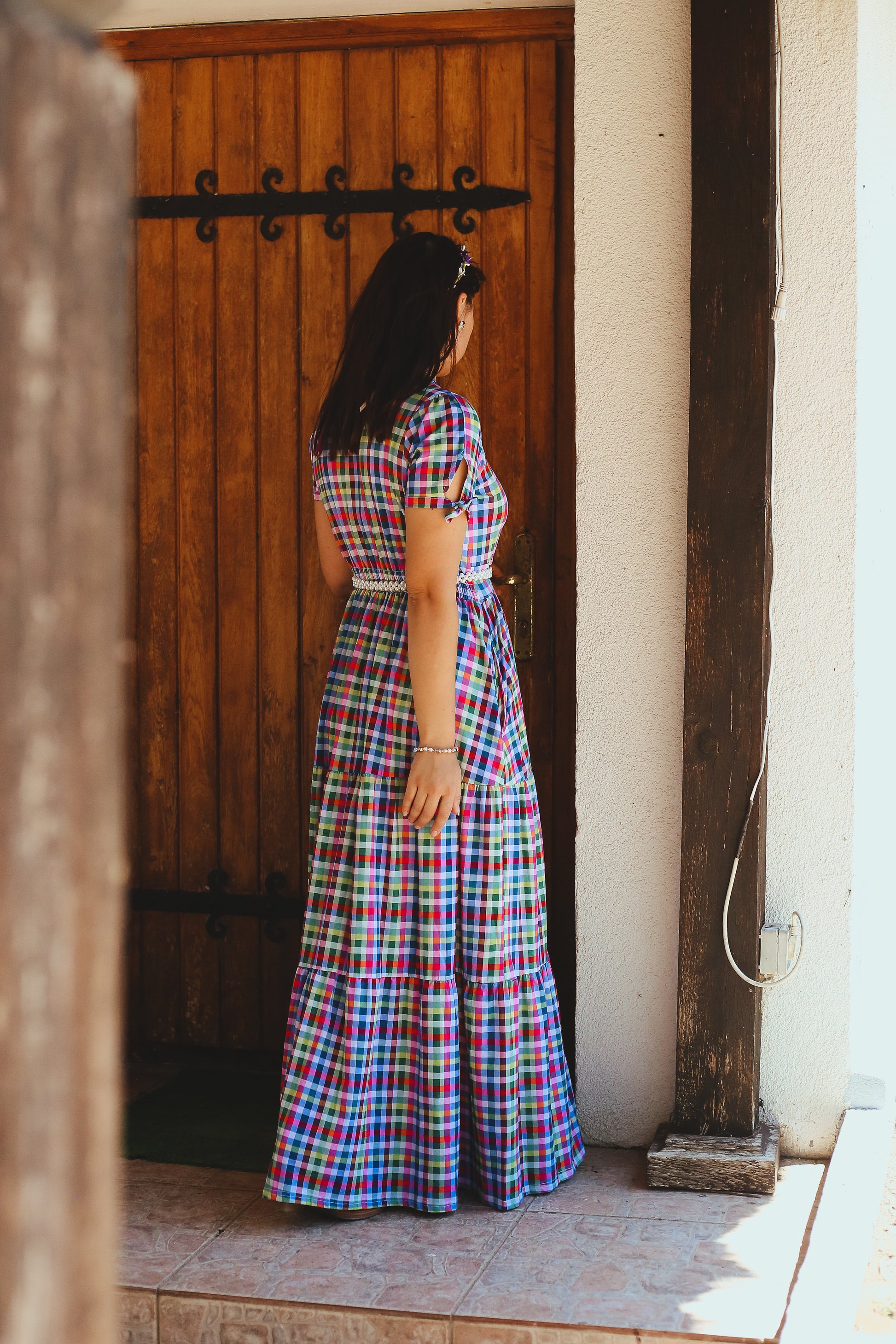 Woman in a colorful modest nursing dress standing in front of a wooden door.