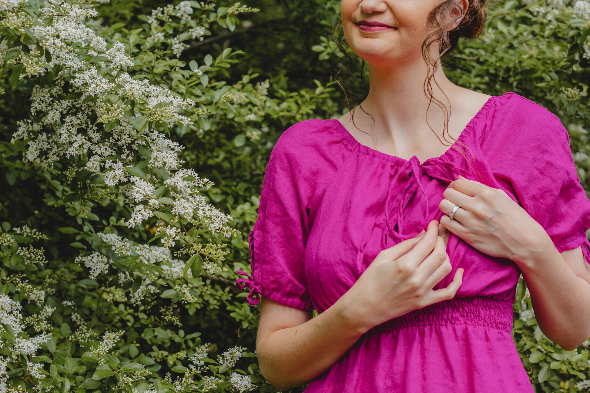Woman in a pink modest nursing dress standing in front of green foliage