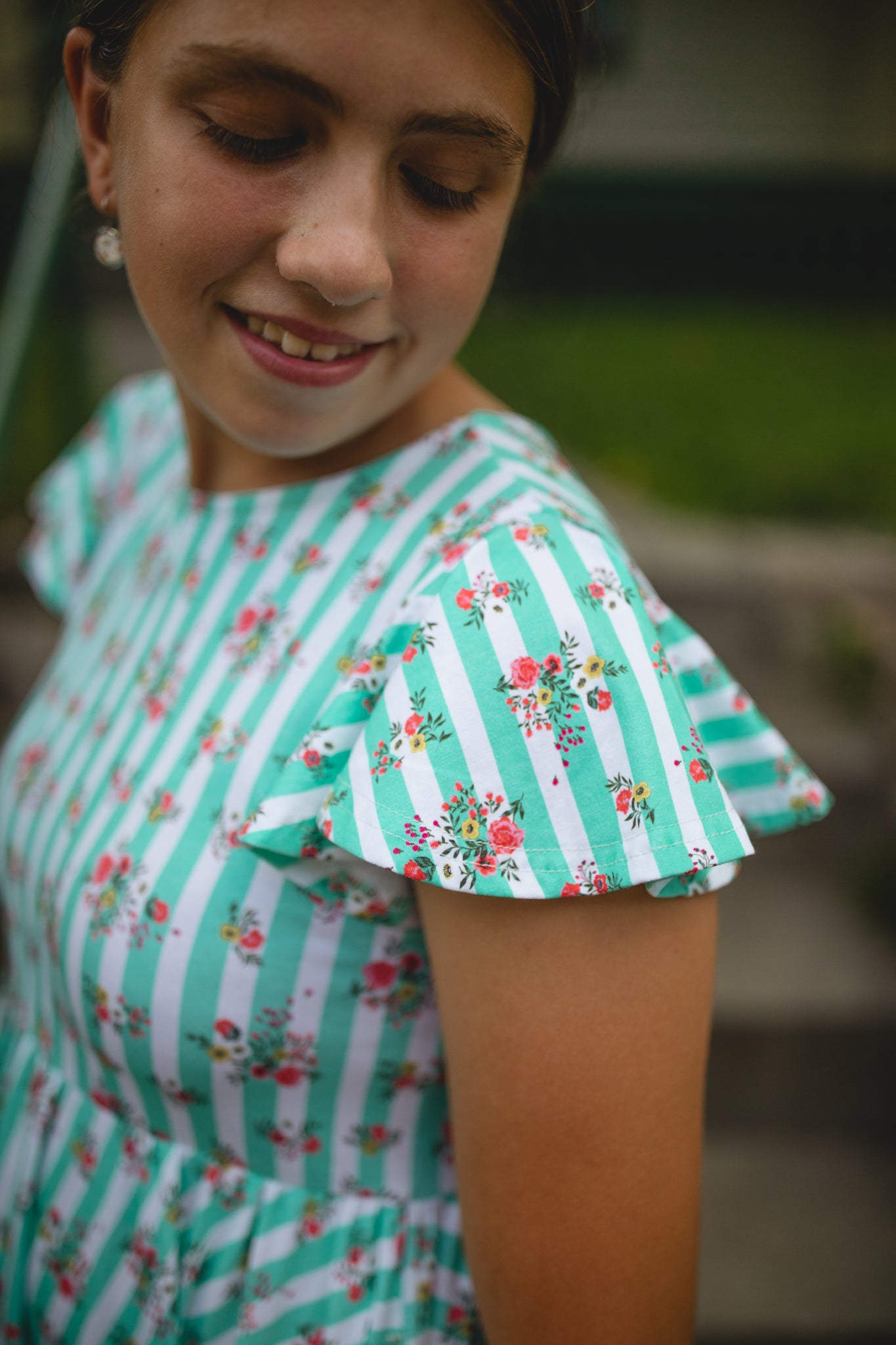 Girl wearing a green and white striped modest dress with floral details on a blurred outdoor background