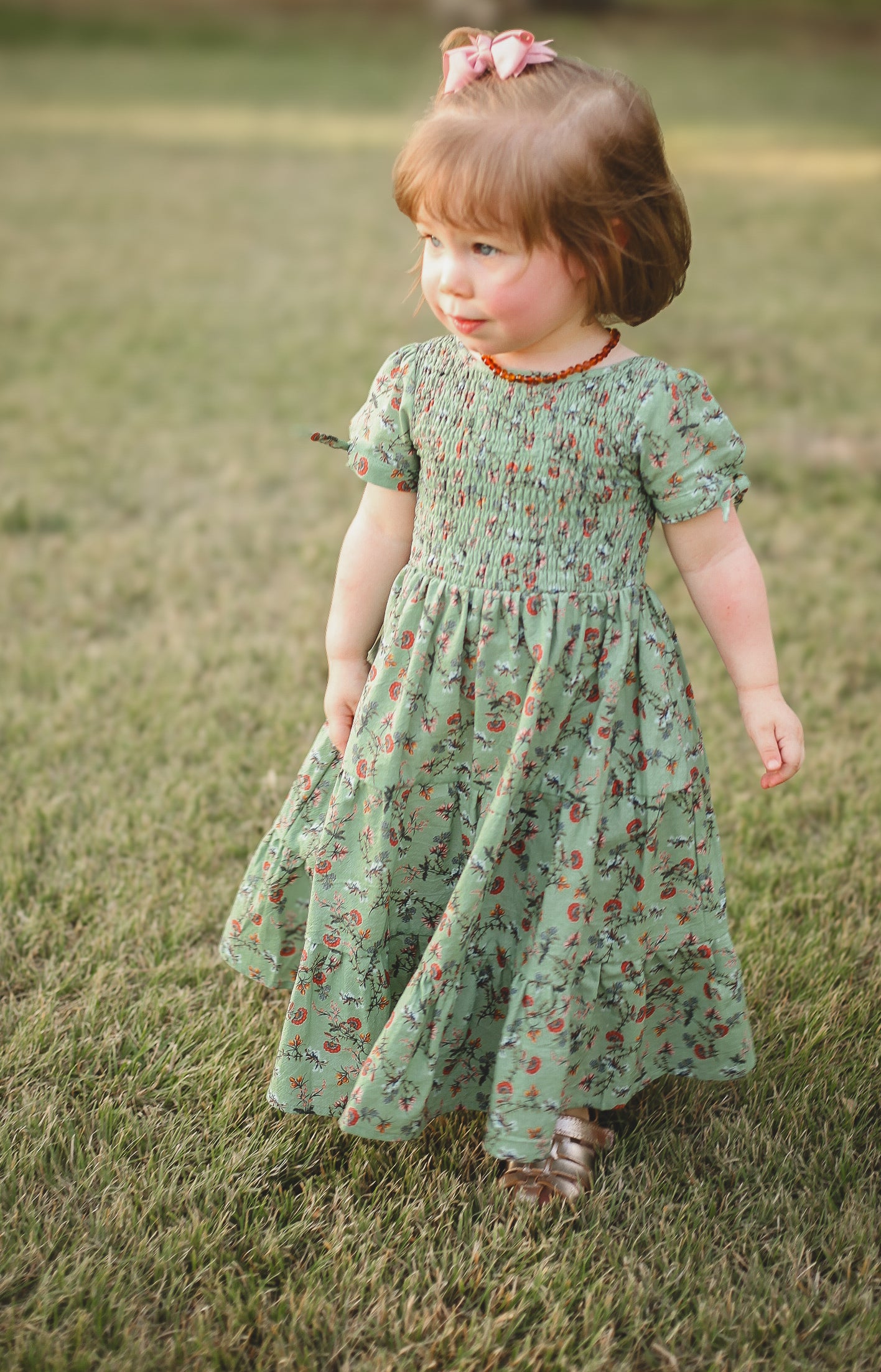 Young girl in a green floral dress standing on grass