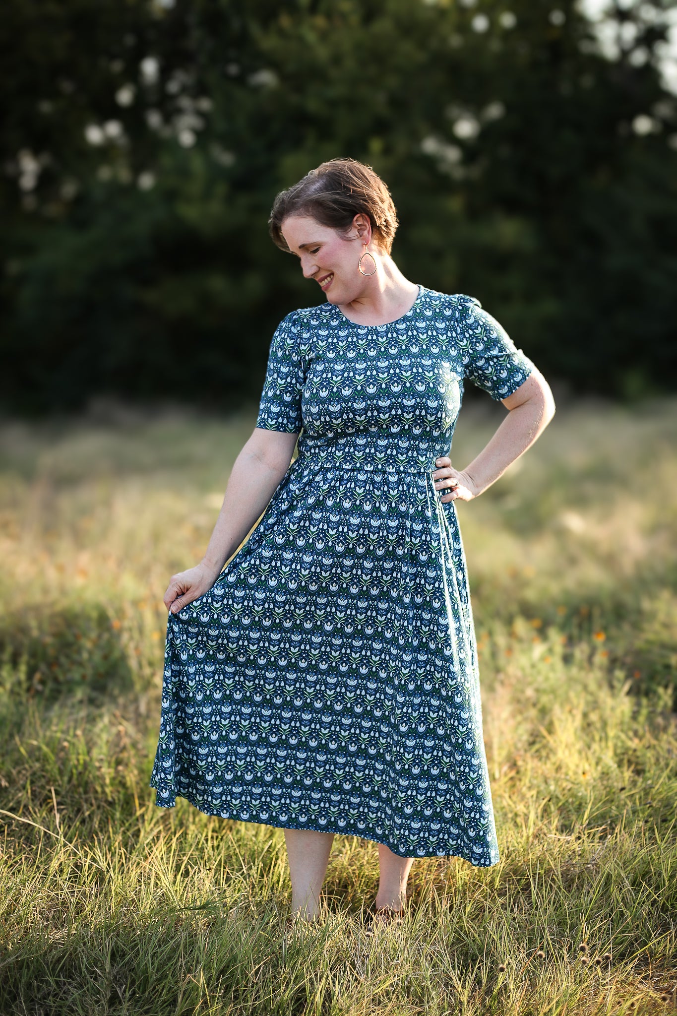 Woman in modest nursing dress, field with trees.