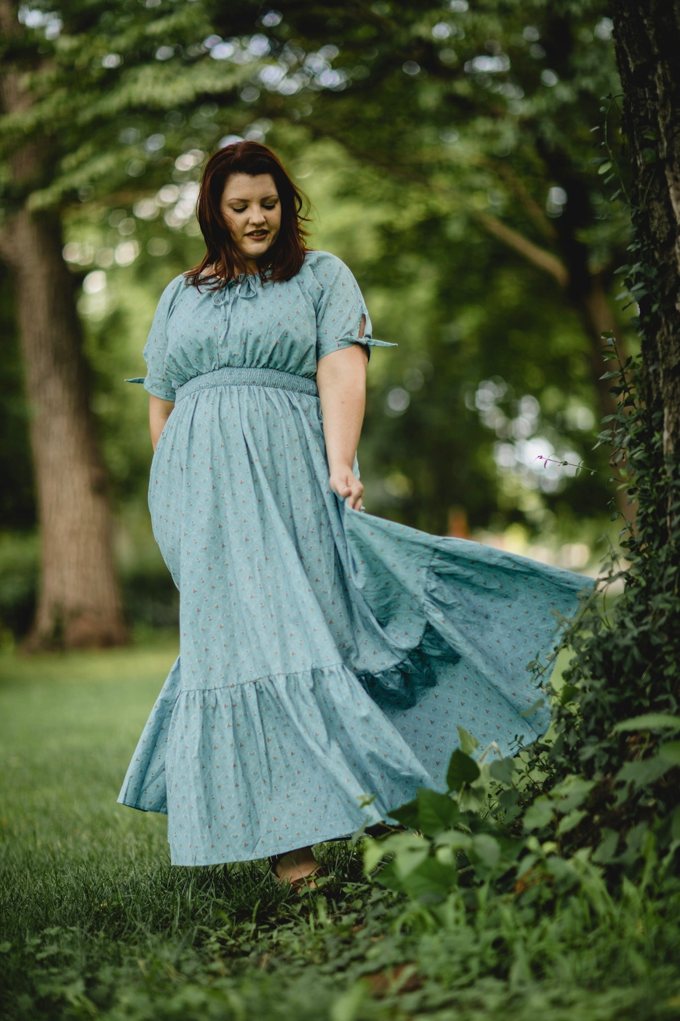 Woman in a light blue modest nursing dress standing in a natural setting with trees and grass.