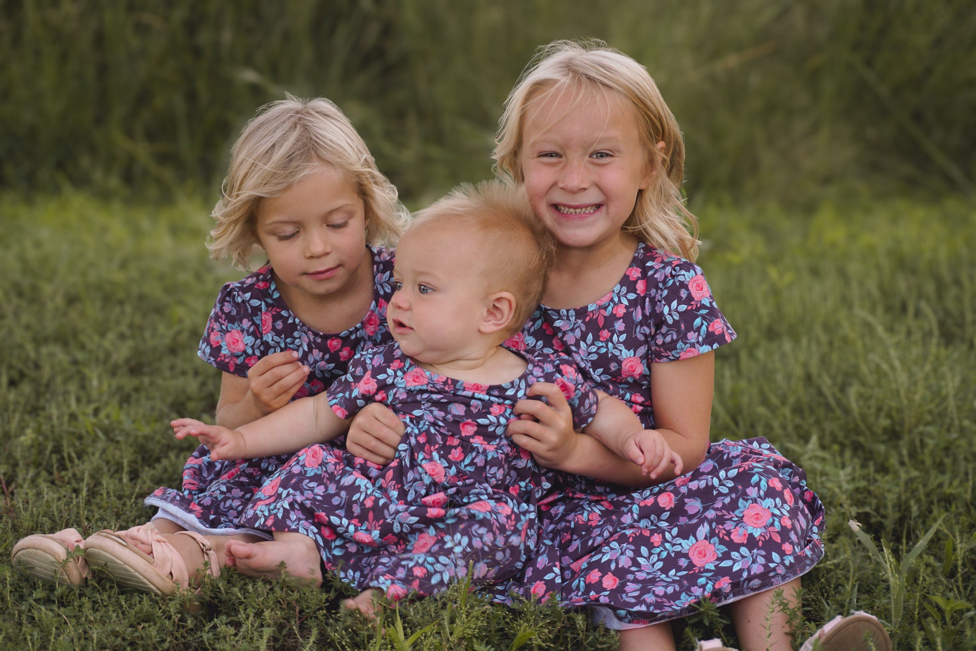 Three girls in matching floral dresses on grass