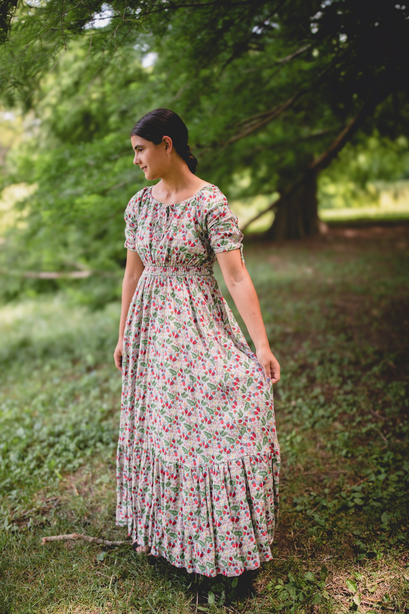 Woman in a floral modest nursing dress standing in a park with trees and grass in the background