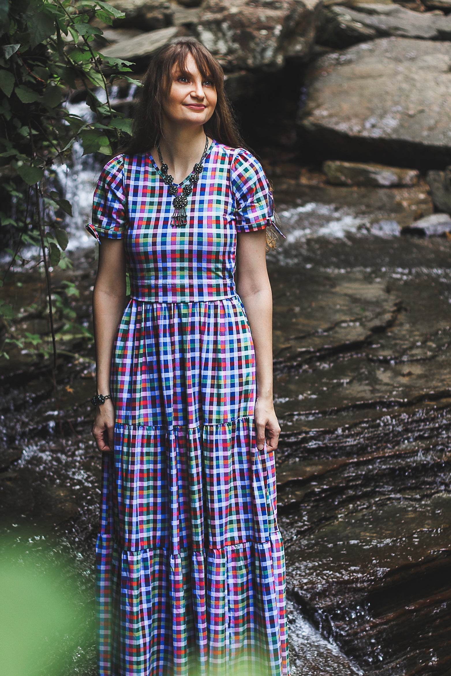 Woman in a colorful checkered modest nursing dress standing by a stream