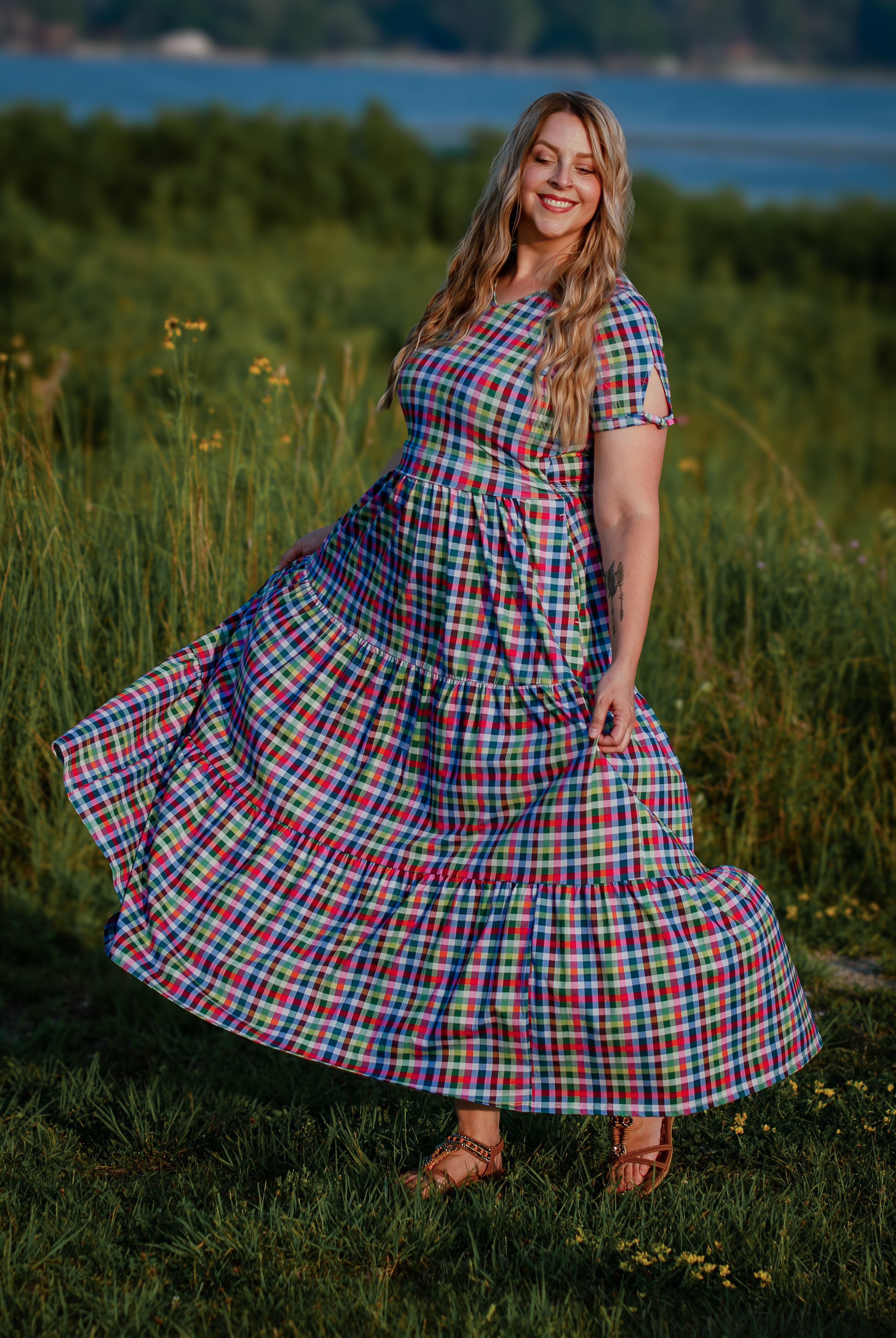 Woman in a plaid modest nursing dress standing in a grassy field with a scenic background