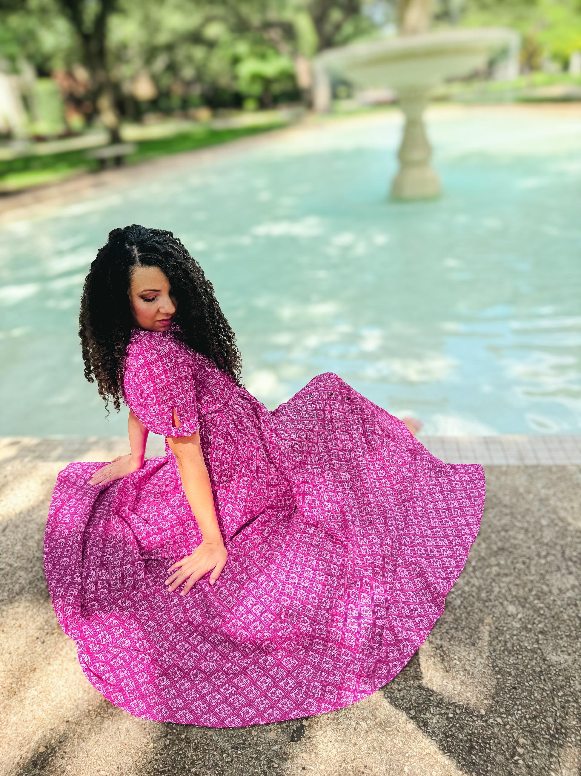 Woman in a pink modest nursing dress sitting by a fountain in a park