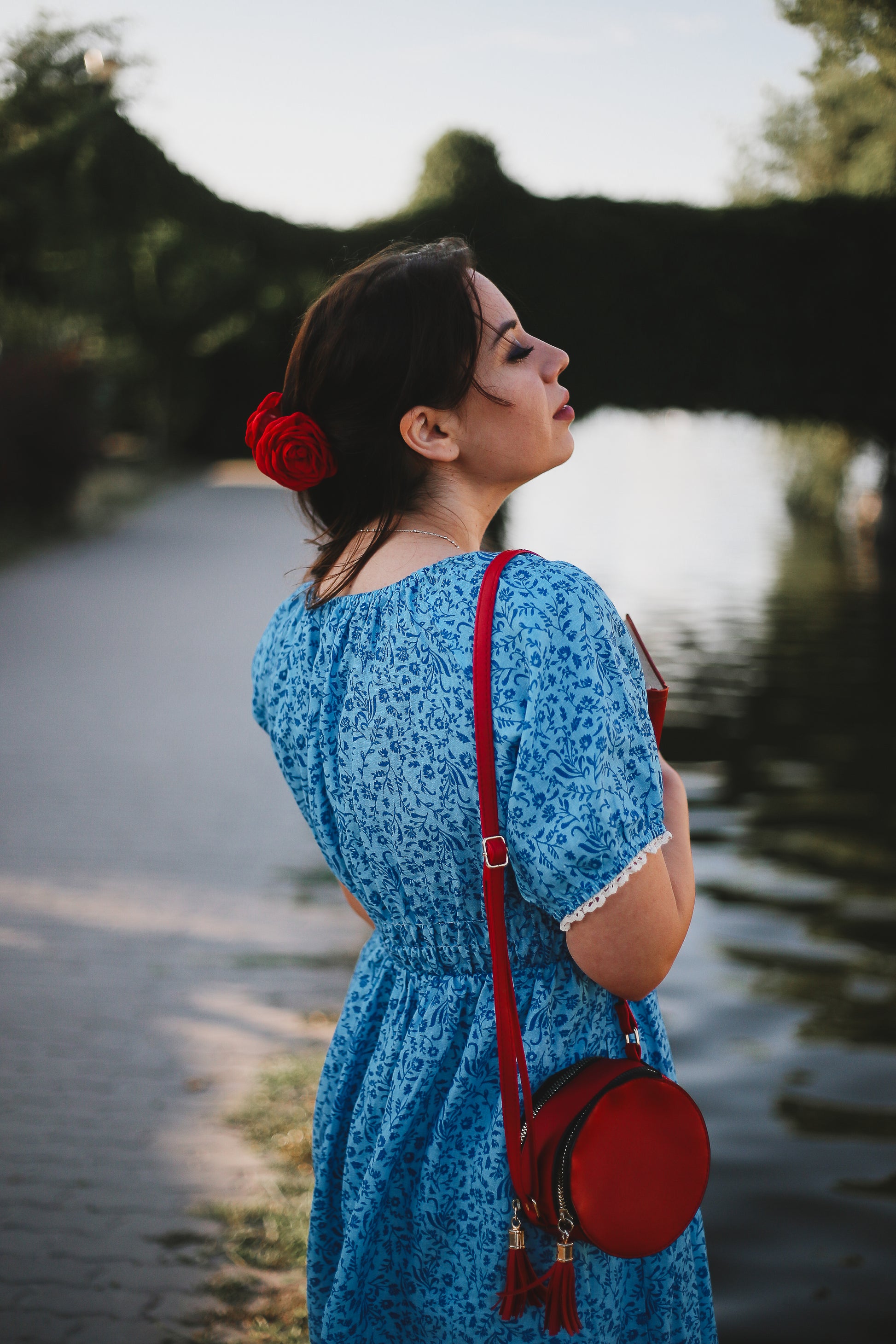 Woman in a blue modest nursing dress with a red bag standing by a water body
