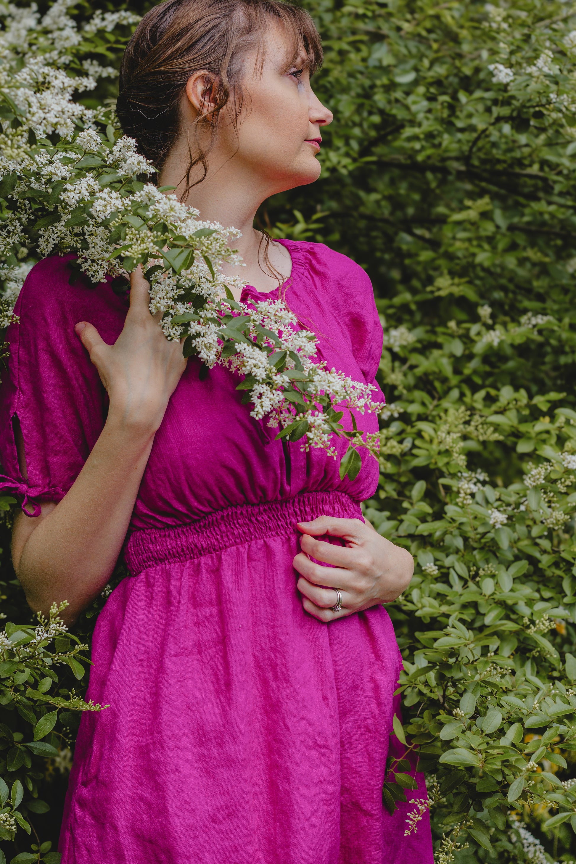 Woman in a pink modest nursing dress holding flowers against a green bush background