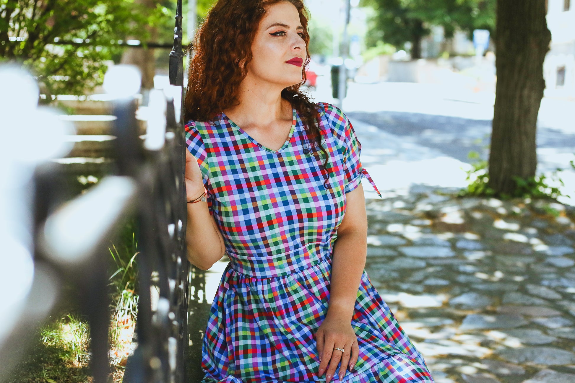 Woman in a colorful checkered modest nursing dress sitting outdoors on a sunny day.