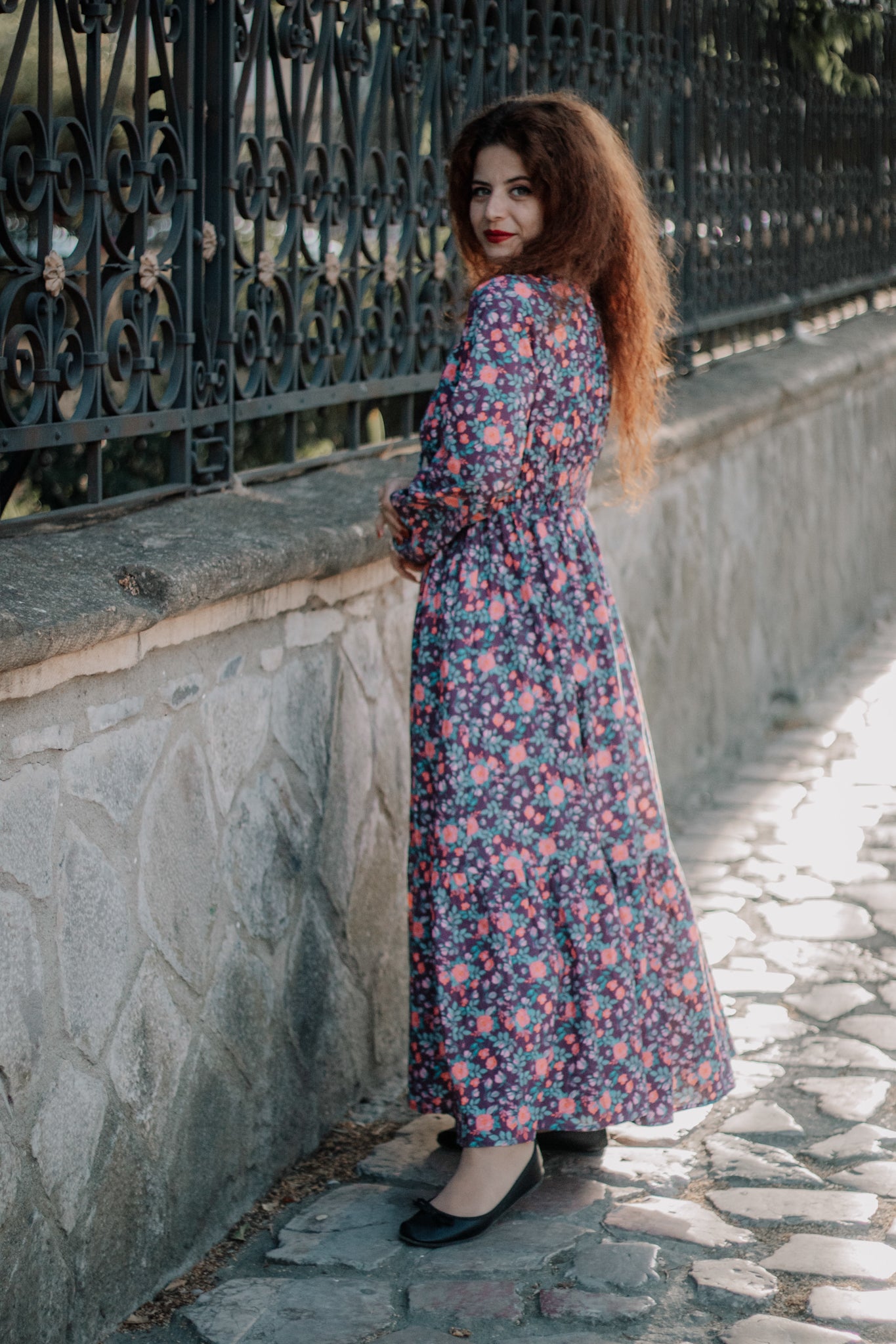 Modest nursing floral dress, woman standing by iron gate.