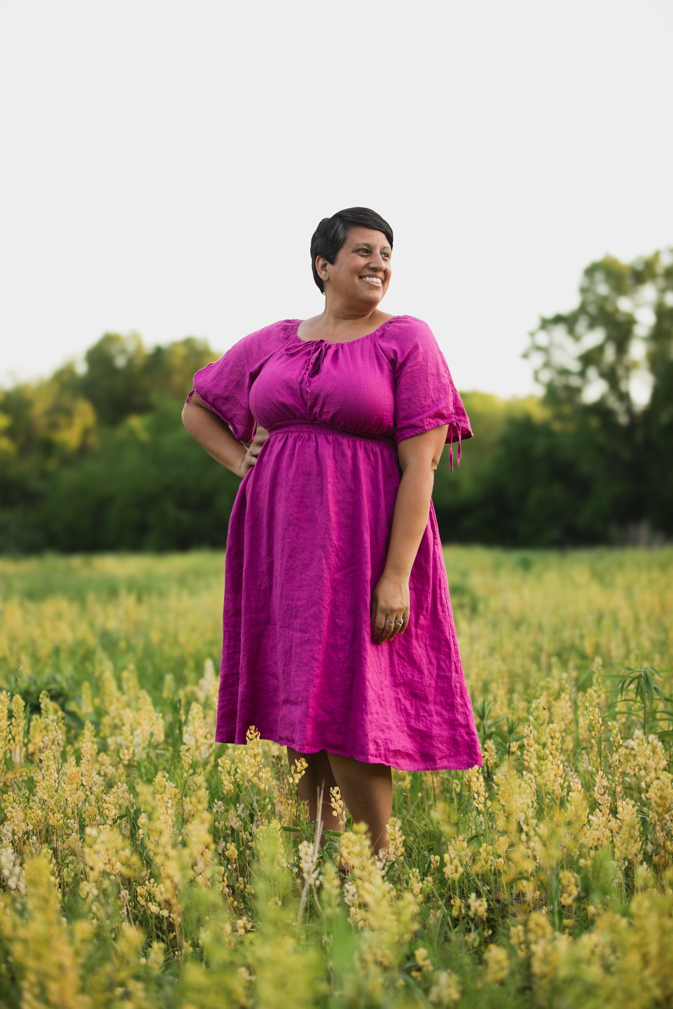 Woman in a pink modest nursing dress standing in a field with trees in the background