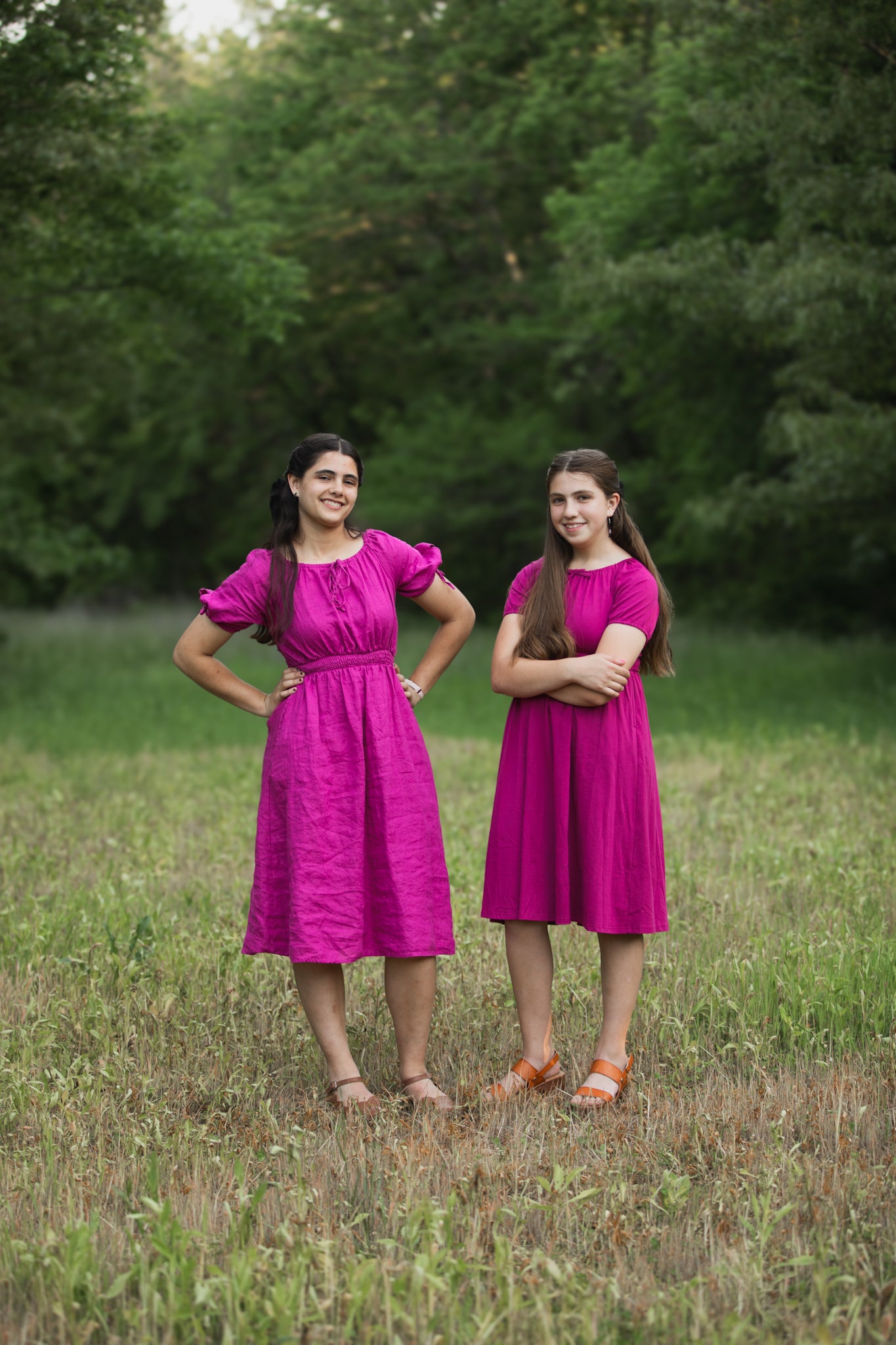 Two women in pink modest dresses standing in a grassy field with trees in the background